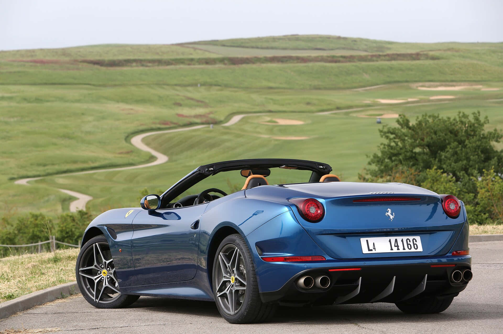 Ferrari California T 桌布 壁紙 — 一輛時尚的藍色法拉利敞篷車停在路邊，俯瞰蜿蜒的綠色高爾夫球場。