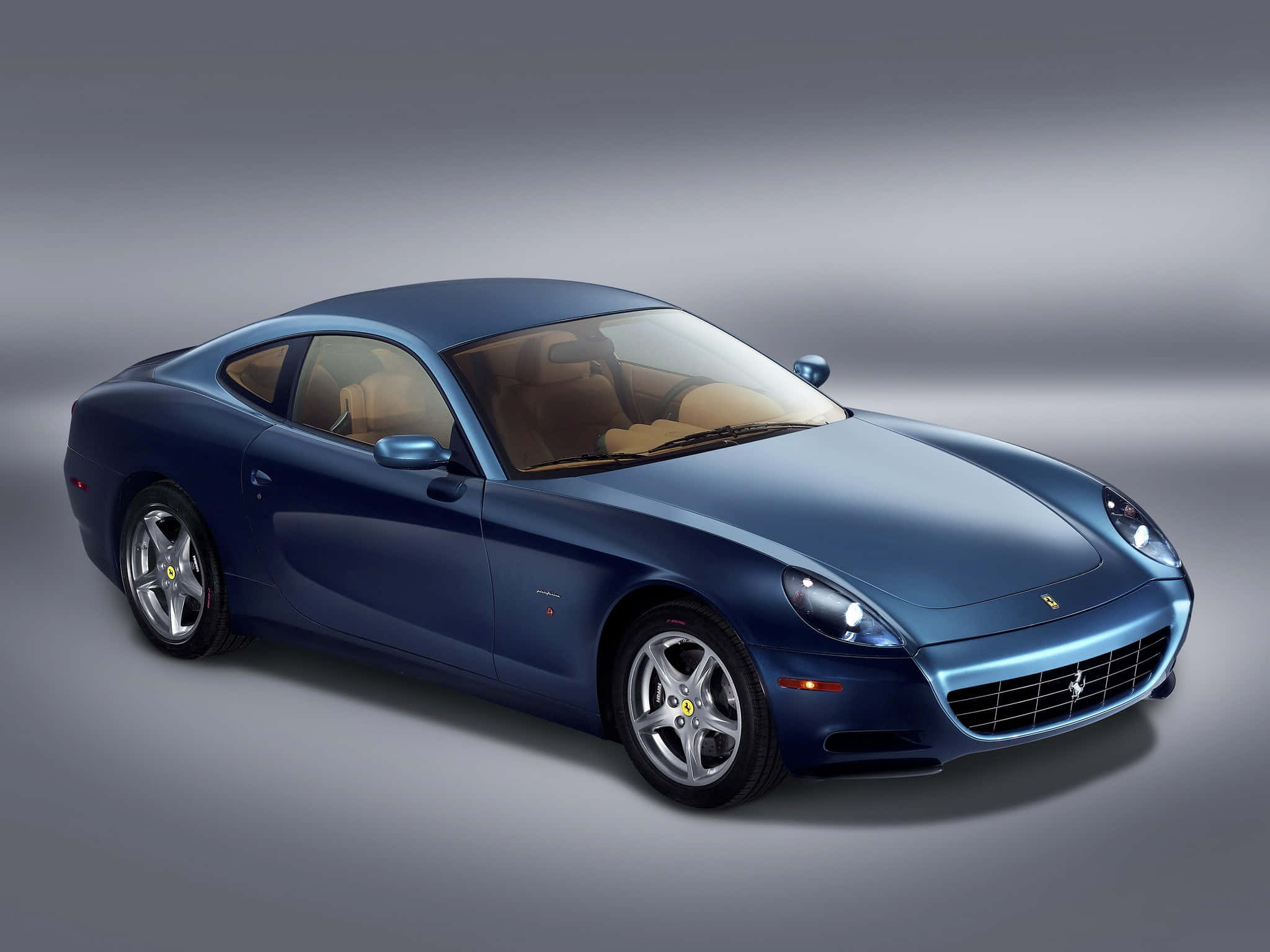 Ferrari 612 Scaglietti 桌布 壁紙 — 一輛時尚的藍色法拉利跑車，配以淺褐色內飾，在柔和漸變燈光的攝影棚環境中展示。
