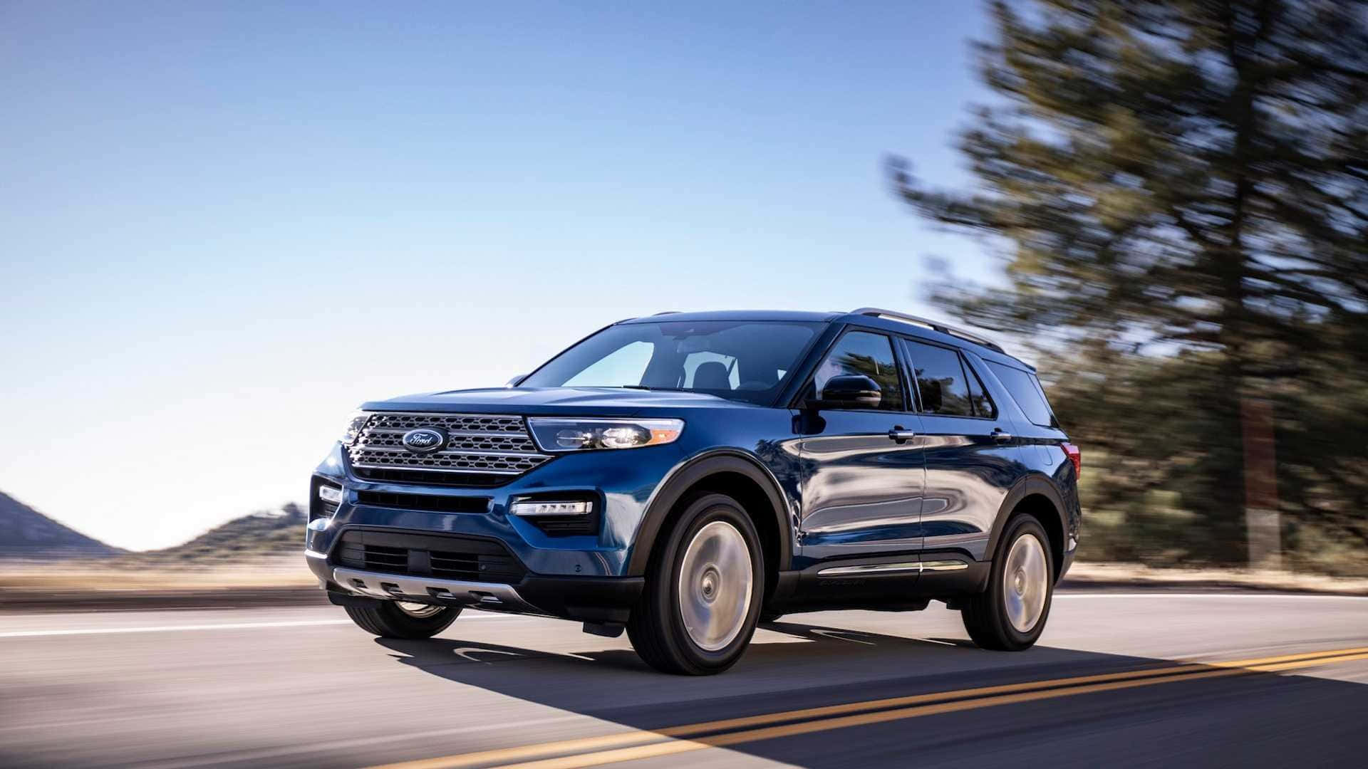 Ford Explorer 桌布 壁紙 — 一輛時尚的藍色福特 Explorer SUV 在陽光明媚的沙漠高速公路上行駛，背景是模糊的樹木和遠處的山脈。