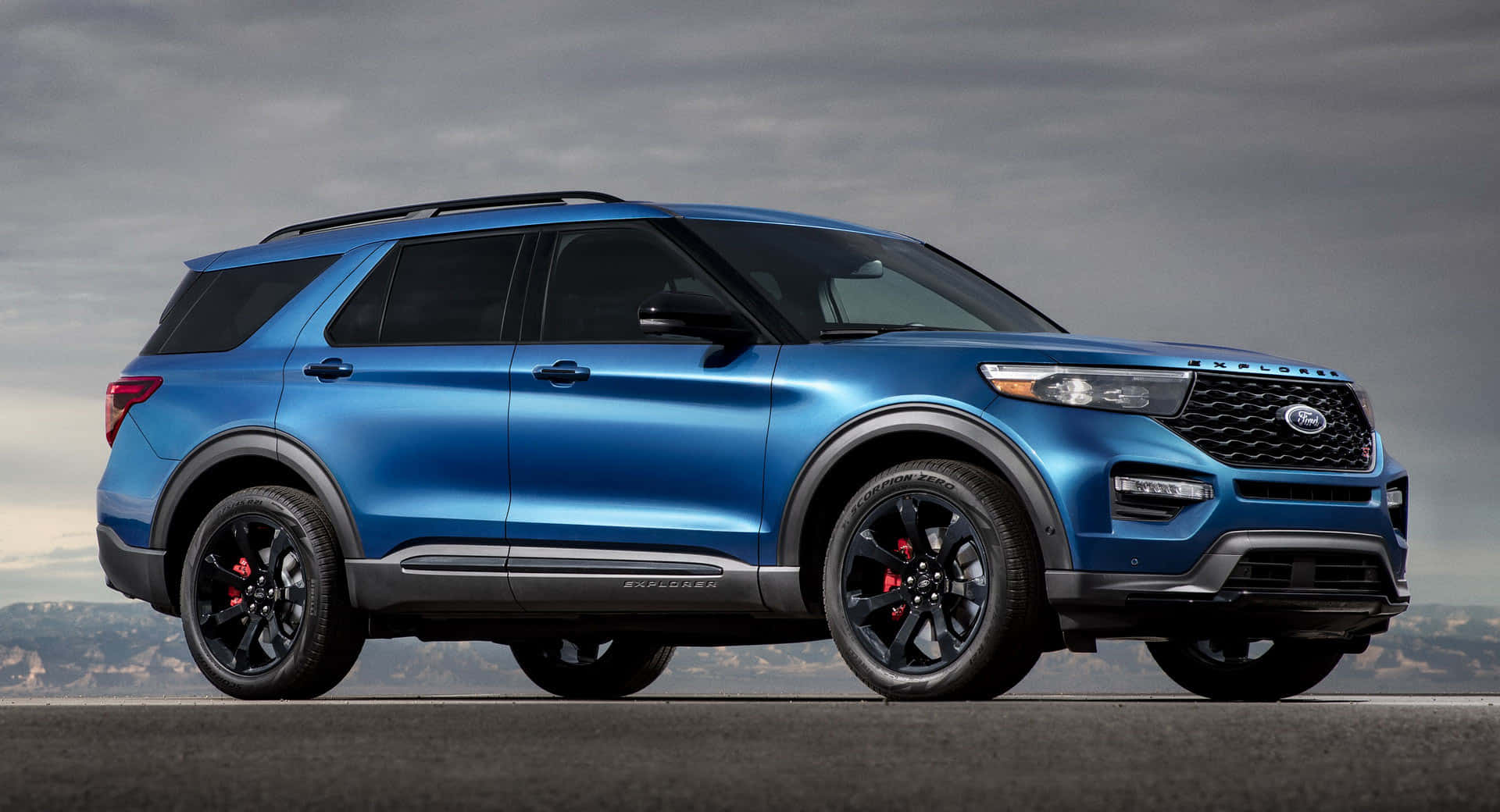Ford Explorer 桌布 壁紙 — 一輛時尚的藍色福特探險者SUV，帶有黑色飾件和紅色制動卡鉗，停在鋪設的道路上，背景是多雲的天空。