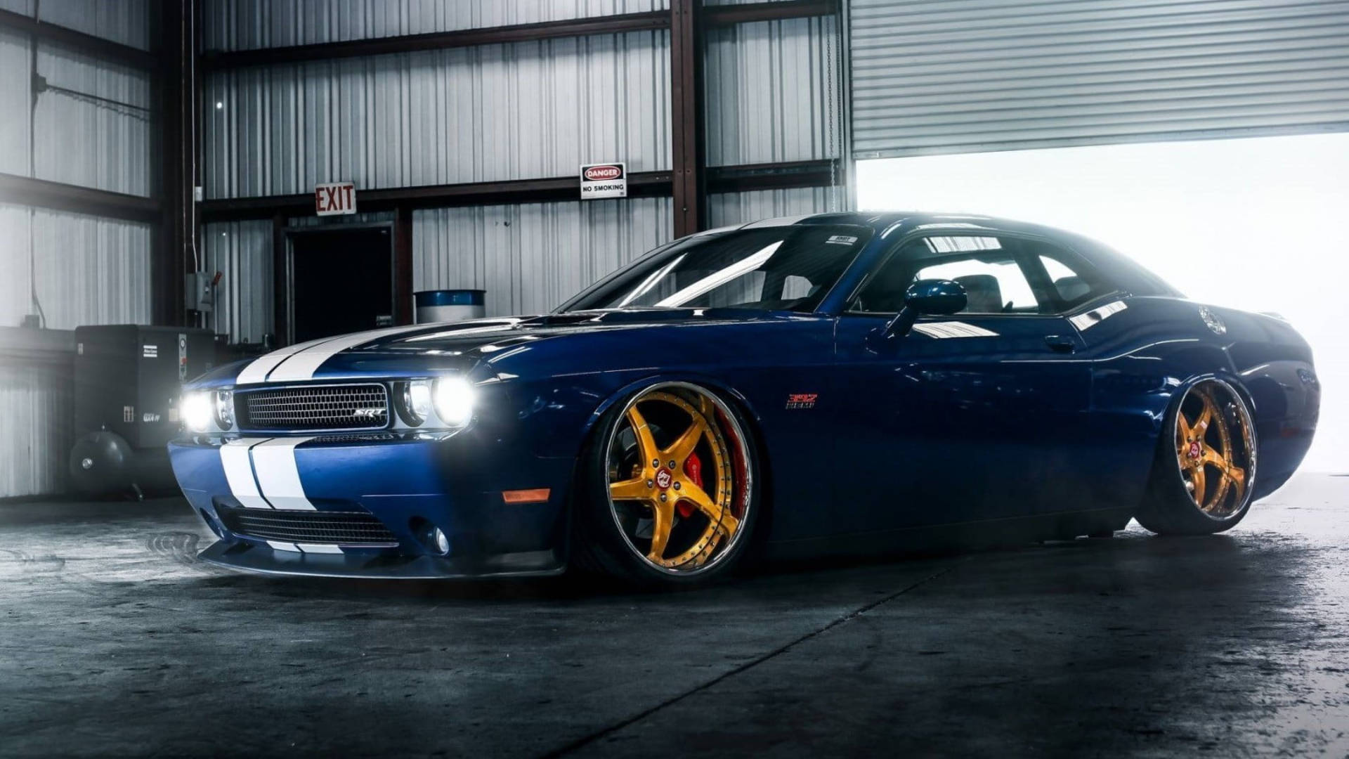 race car 桌布 壁紙 — 一輛時尚的藍色肌肉車，配金色輪圈和白色條紋，在金屬倉庫內的明亮燈光下閃閃發光。
