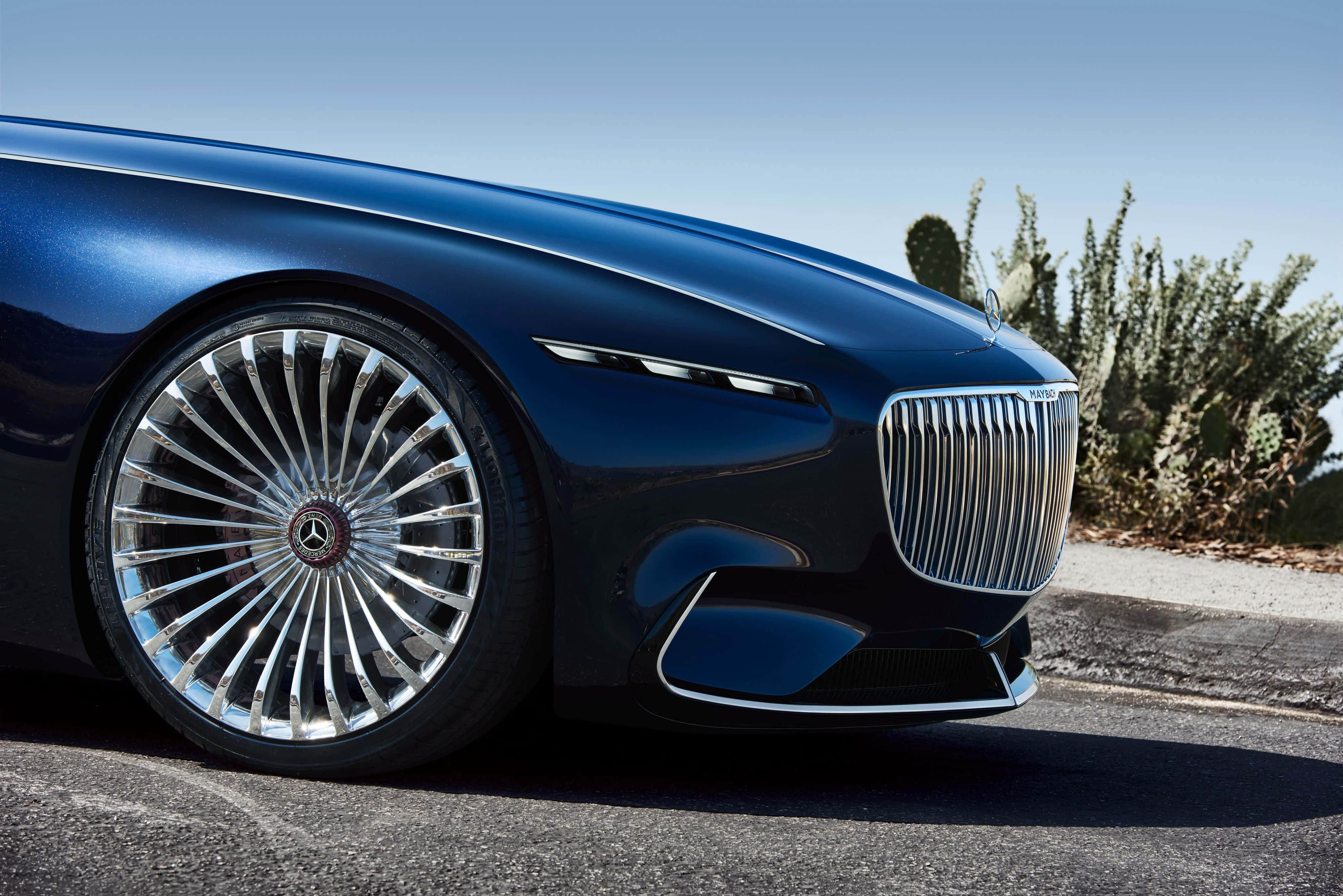 Maybach 桌布 壁紙 — 一輛時尚的藍色豪華車，帶有精緻的鍍鉻輪圈，在明亮的日光下停在瀝青路上，旁邊是沙漠仙人掌。