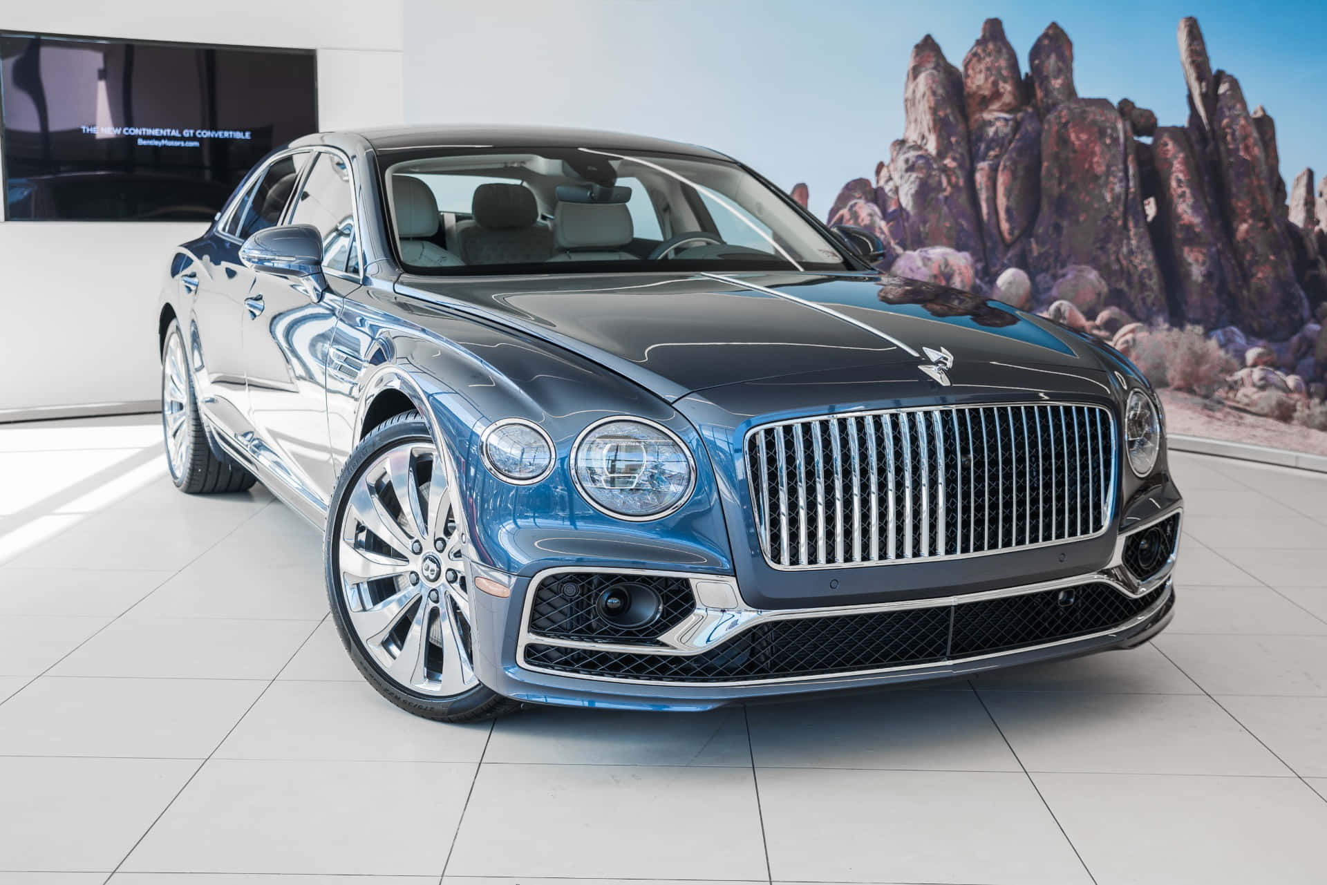 Bentley Flying Spur 桌布 壁紙 — 一輛時尚的藍色賓利 Continental GT Convertible 在現代展廳中，以沙漠岩石壁畫為背景，在明亮燈光下閃閃發光。