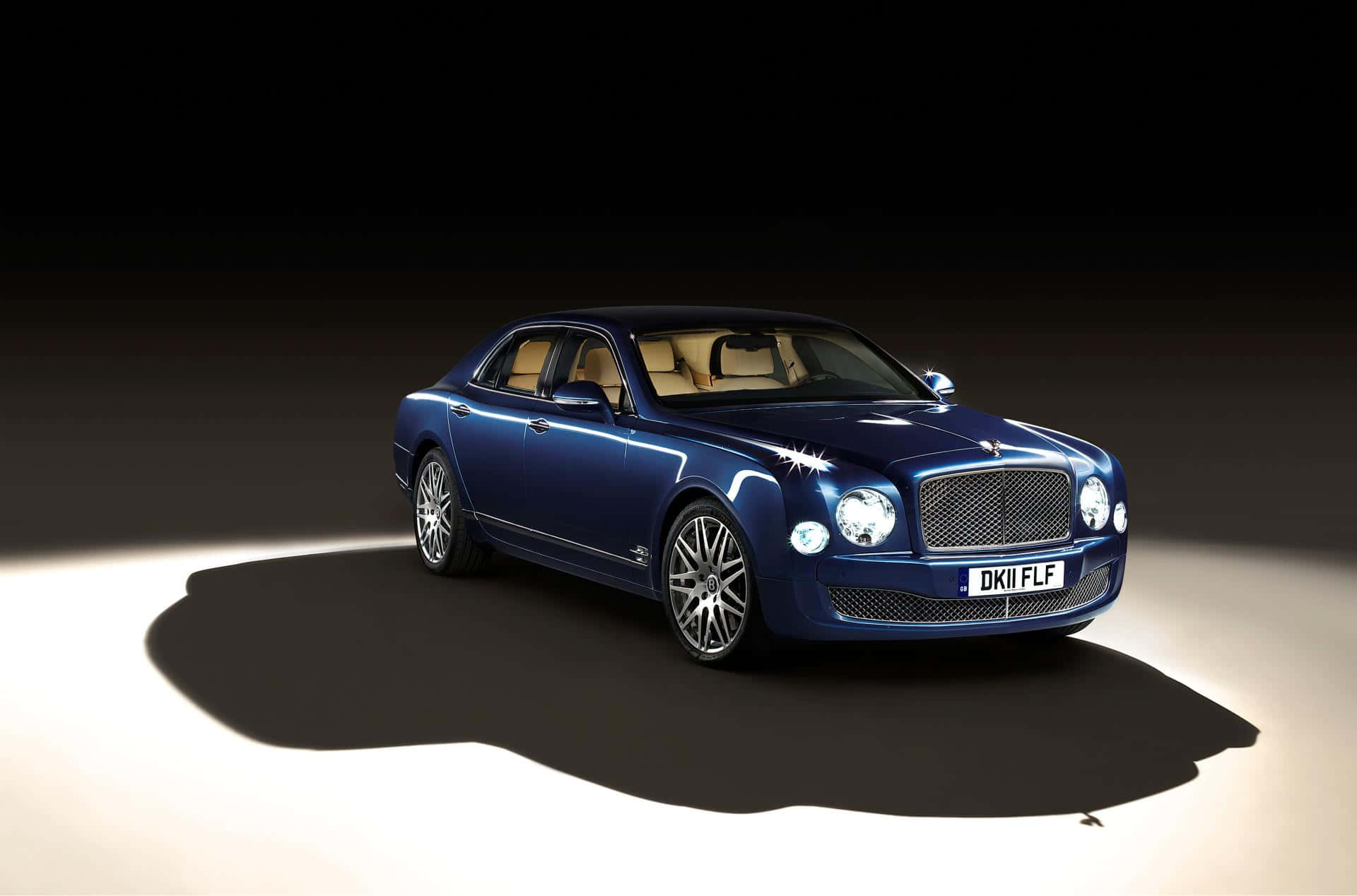 Bentley Mulsanne 桌布 壁紙 — 一輛時尚的藍色賓利轎車在戲劇性的聚光燈下閃閃發光，背景是黑暗的工作室，並帶有長長的陰影。