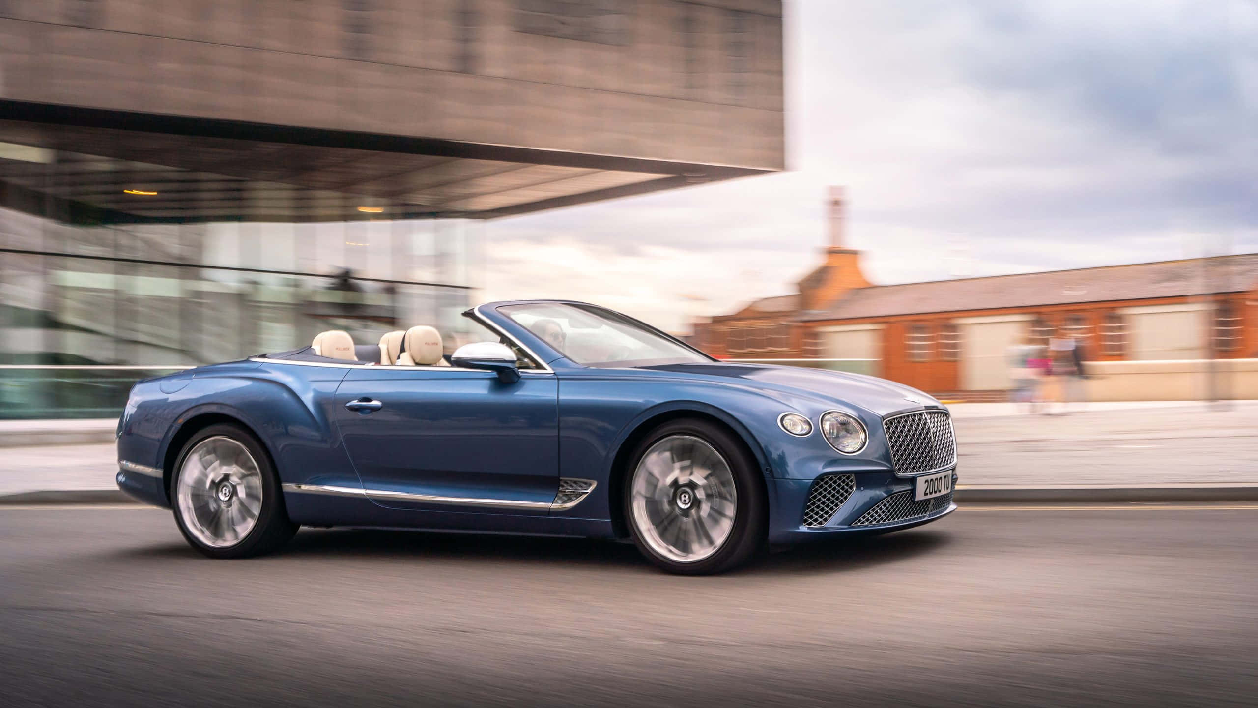 Bentley Continental Gt 桌布 壁紙 — 一輛時尚的藍色賓利開篷跑車在現代城市街道上飛馳，背景呈現動態模糊效果。