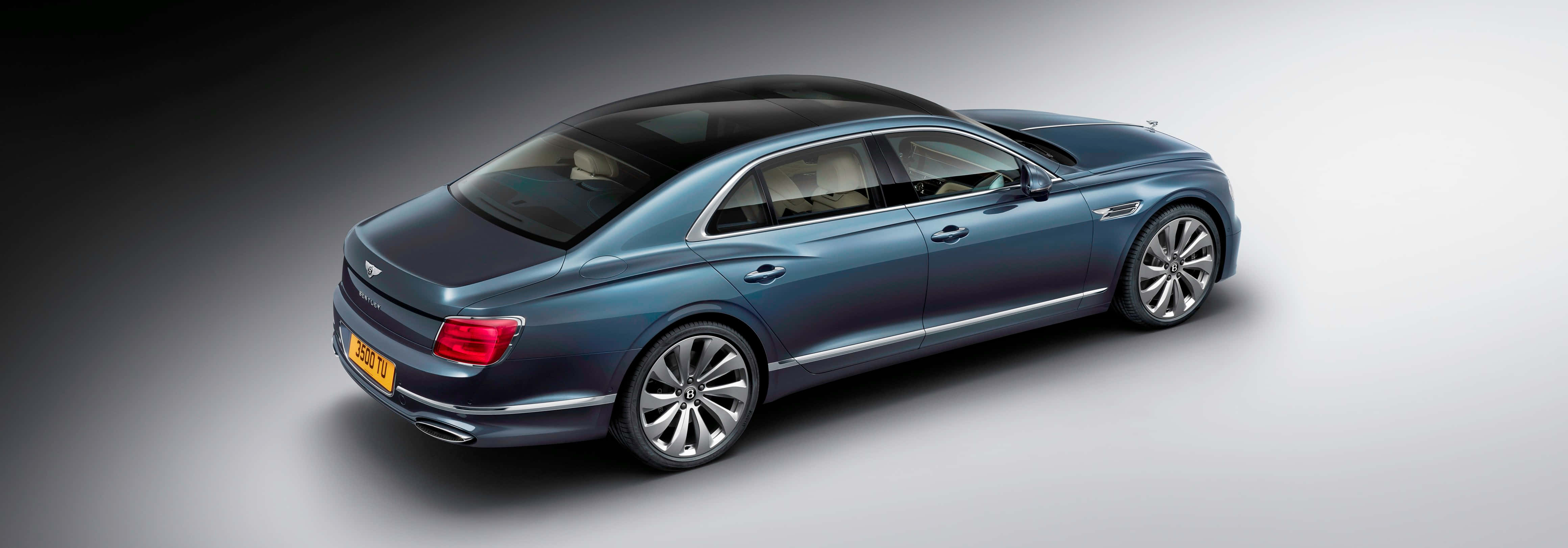 Bentley Flying Spur 桌布 壁紙 — 一輛時尚的藍色賓利飛馳轎車在極簡灰色背景的攝影棚燈光下閃閃發光。