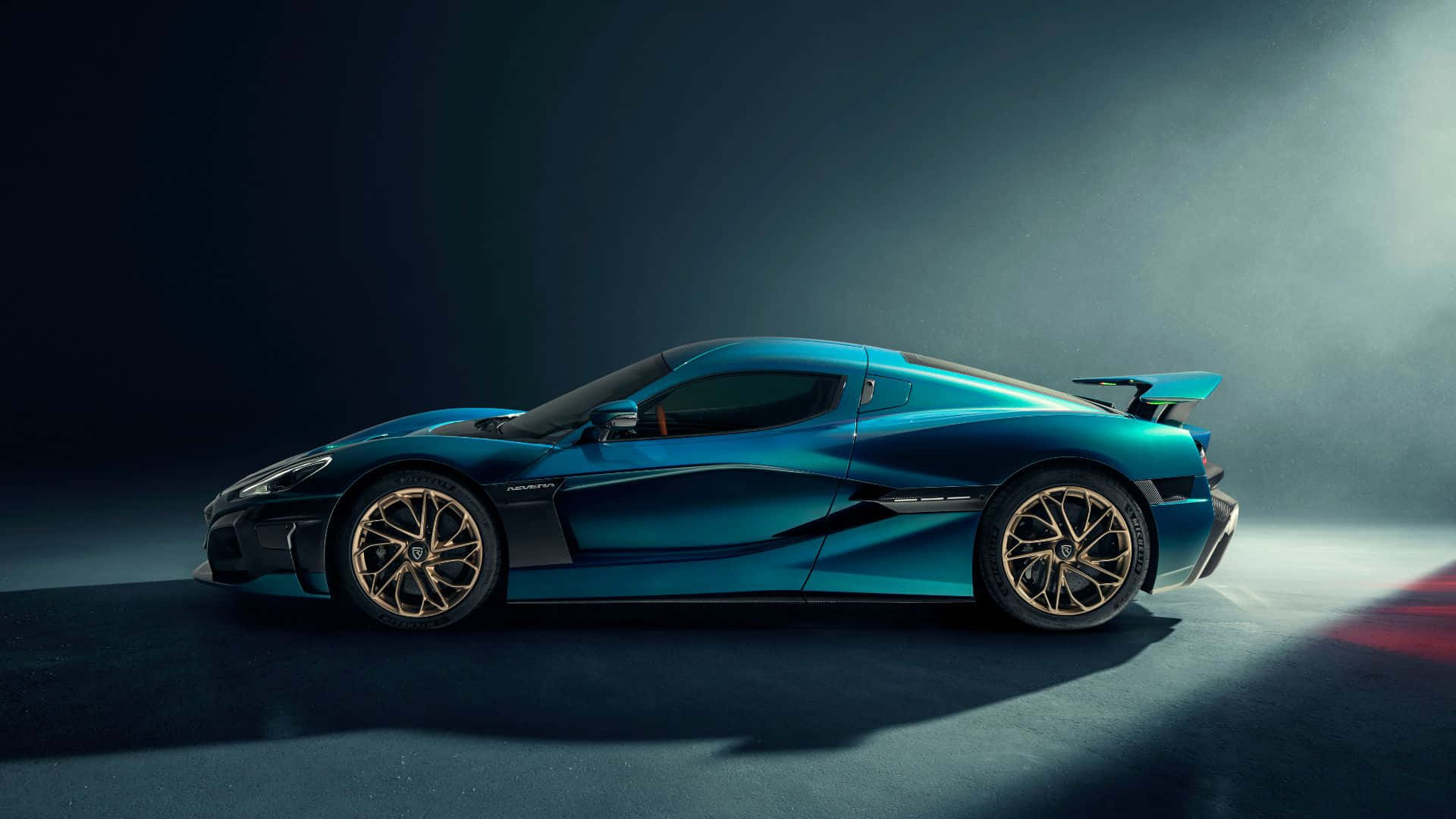 Rimac 桌布 壁紙 — 一輛時尚的藍色超級跑車配金色輪圈，在戲劇性的攝影棚燈光下閃耀，在深色地板上投下長長的陰影。