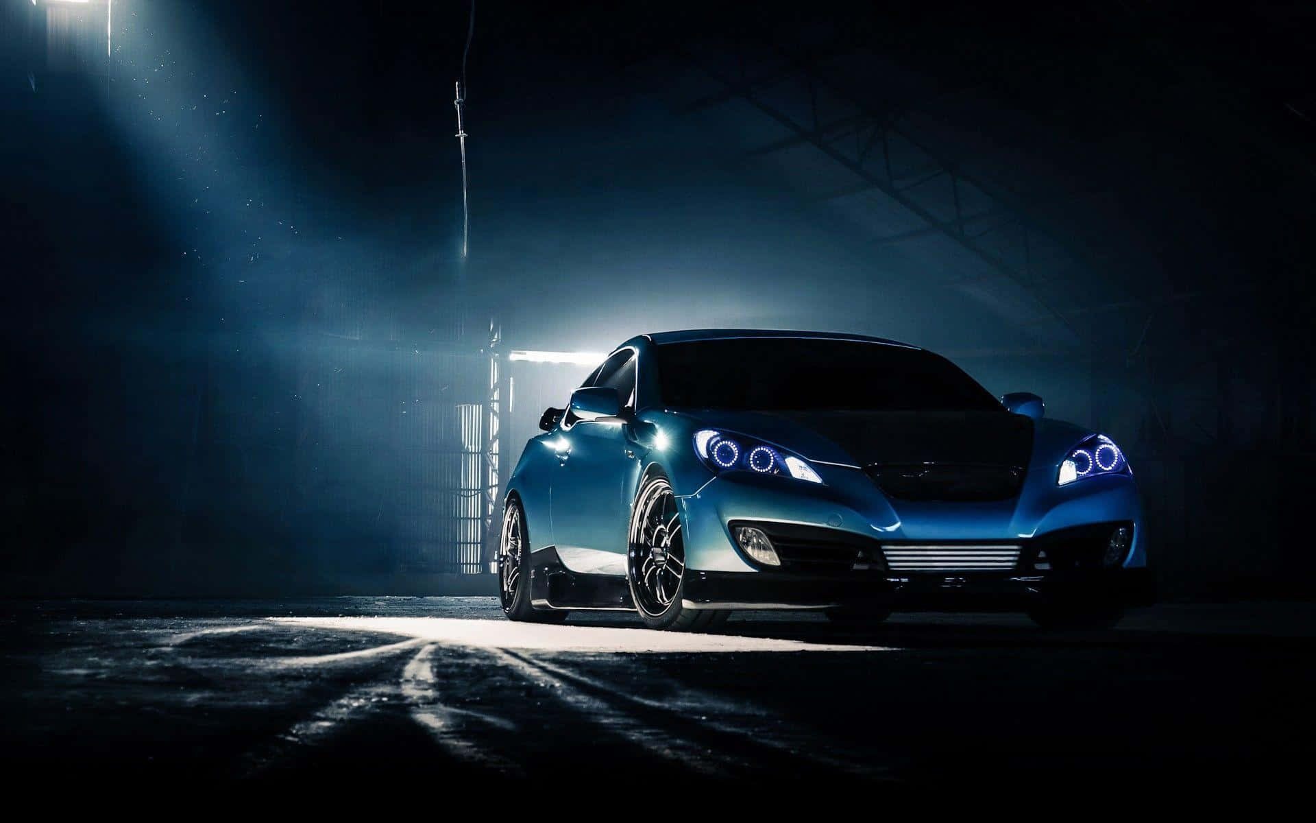 Hyundai Tiburon 桌布 壁紙 — 一輛時尚的藍色跑車在夜間霧濛濛的工業倉庫中，在戲劇性的聚光燈下發光。