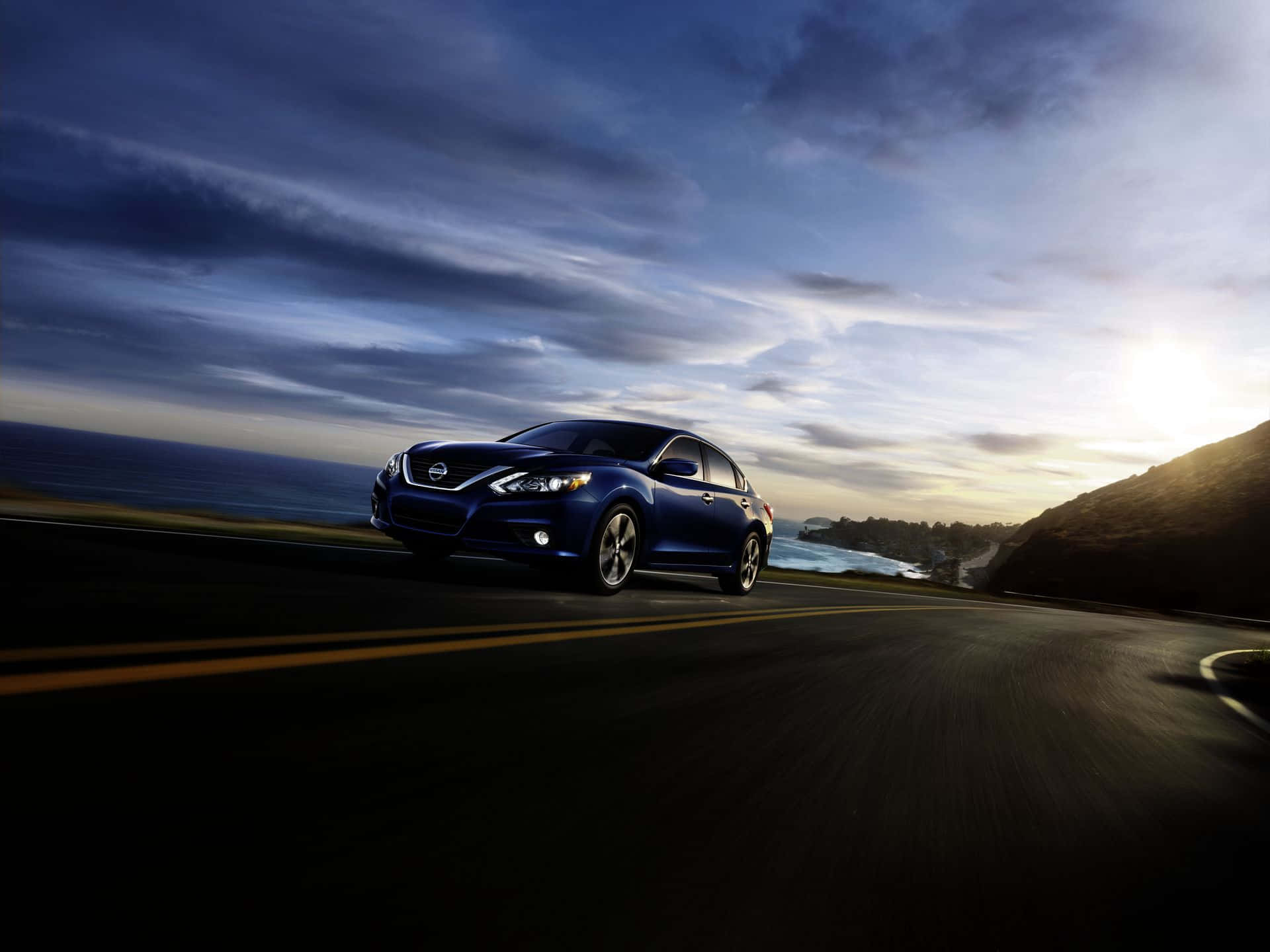 Nissan Altima 桌布 壁紙 — 一輛時尚的藍色轎車在日落時分沿著海岸公路飛馳，背景是海洋和懸崖。