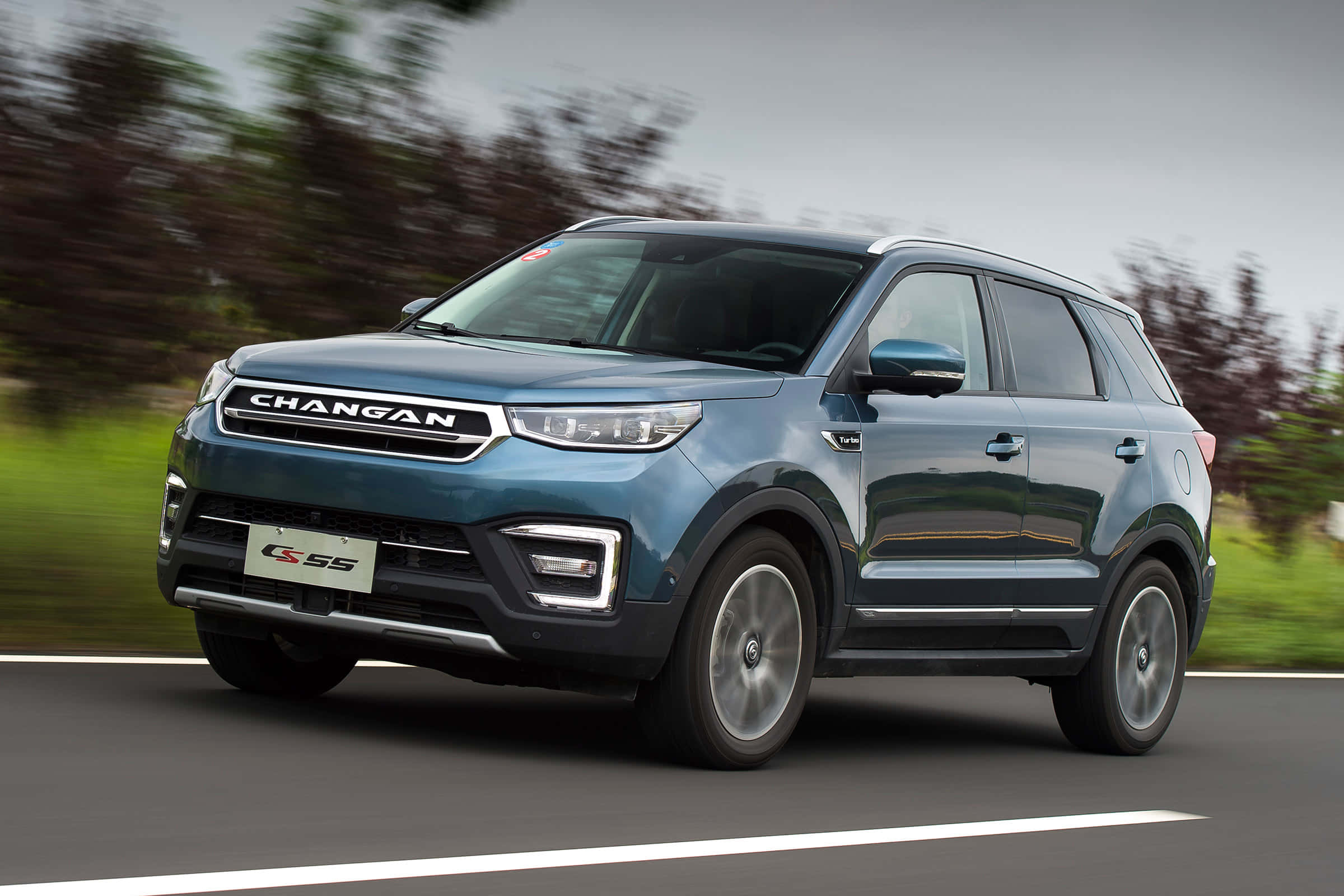 Changan 桌布 壁紙 — 一輛時尚的藍色長安CS55 SUV在道路上疾馳，背景是模糊的綠植。