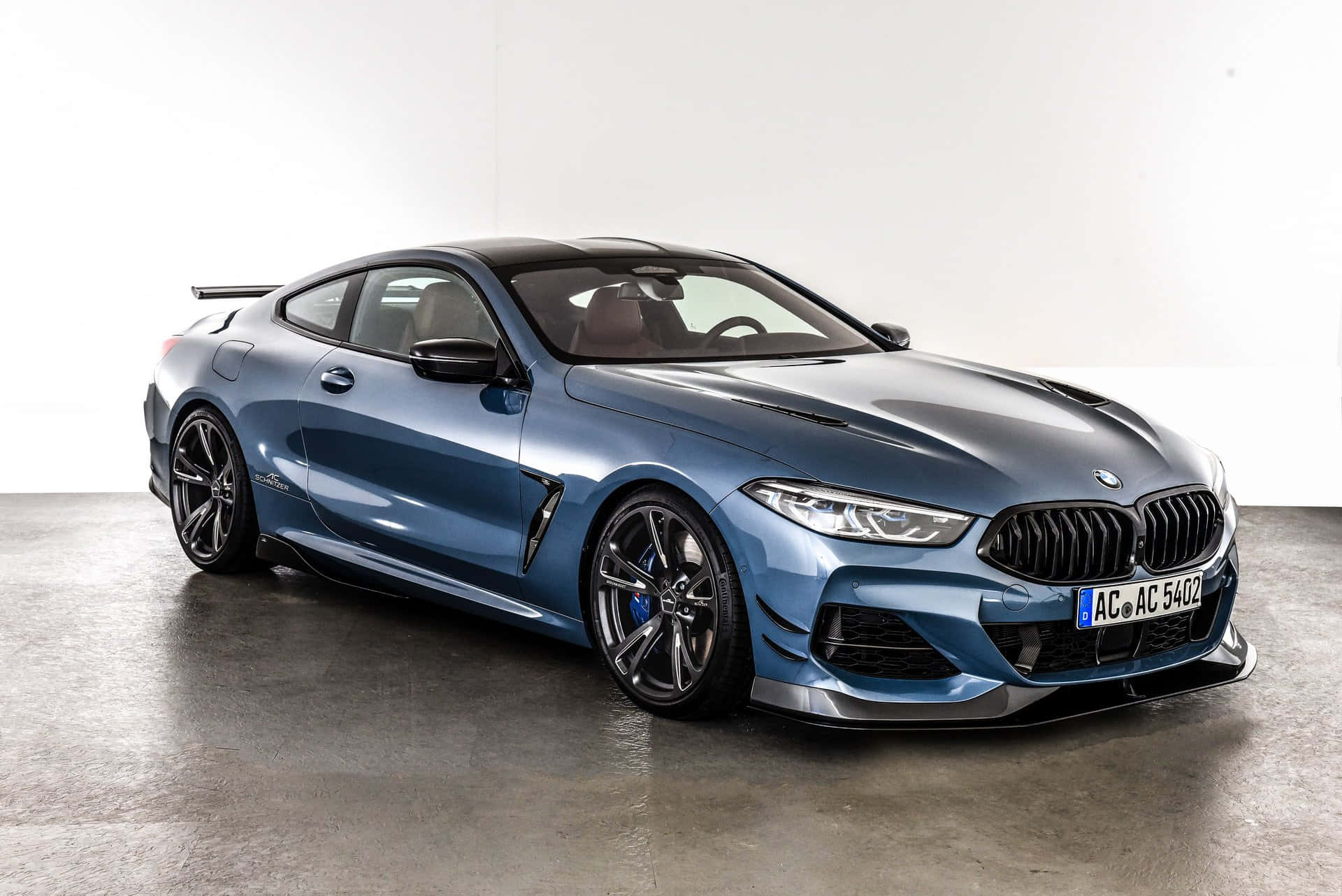 Bmw 8 Series 桌布 壁紙 — 一輛時尚的金屬藍色BMW M8 Coupe，帶有黑色飾邊和定制輪圈，置於簡約工作室環境中。