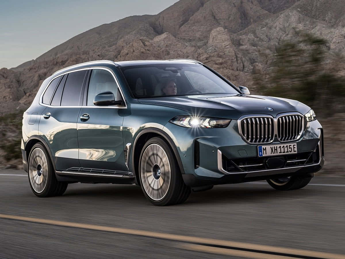 Bmw X5 桌布 壁紙 — 一輛時尚的金屬藍色BMW X5 SUV在沙漠公路上飛馳，背景是崎嶇的山脈。