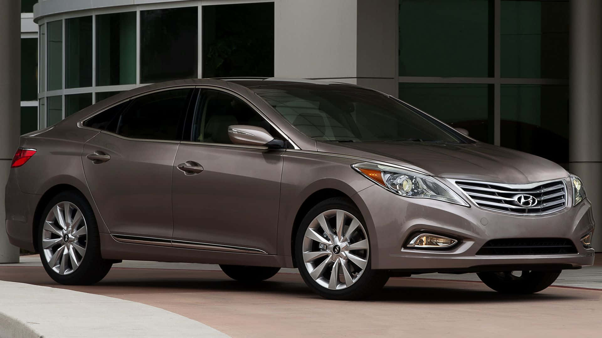 Hyundai Azera 桌布 壁紙 — 一輛時尚的銀灰色現代轎車停在現代玻璃建築前，線條簡潔，合金輪轂拋光。
