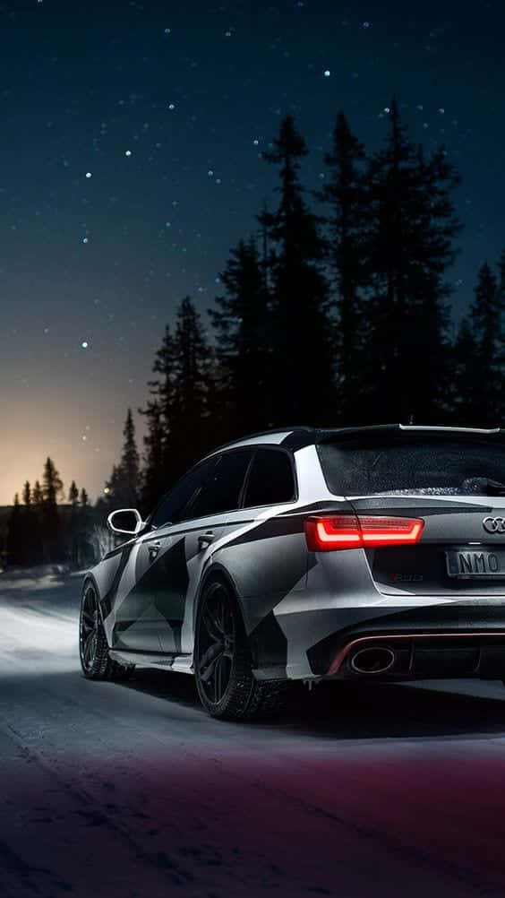  壁紙 — 一輛時尚的銀色 Audi 旅行車在星空下駛過白雪覆蓋的樹林，紅色尾燈閃爍發光。