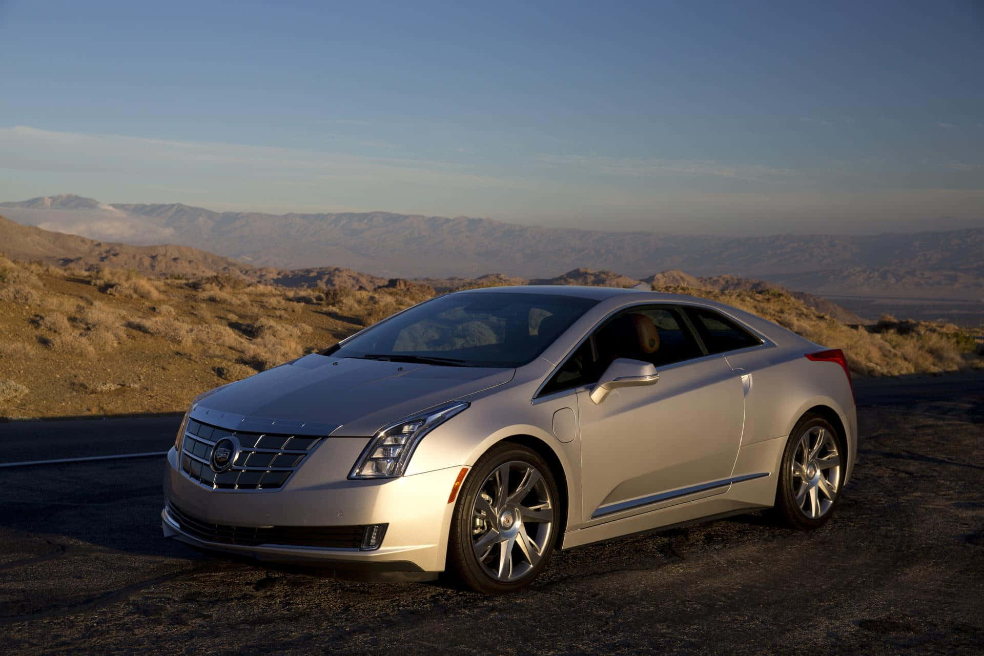 Cadillac Elr 桌布 壁紙 — 一輛時尚的銀色 Cadillac ELR 電動雙門跑車停在沙漠公路上，遠處有山脈，天空清澈湛藍。