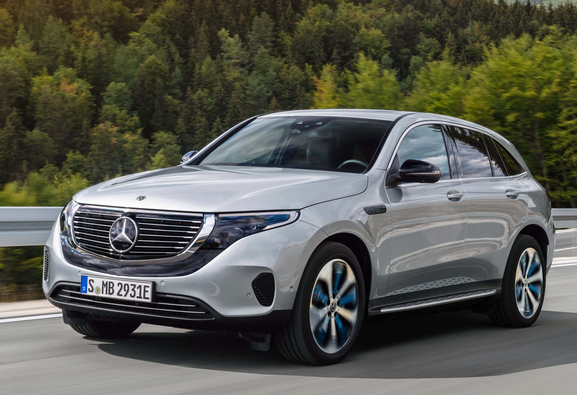 Mercedes Benz Eqc 桌布 壁紙 — 一輛時尚的銀色 Mercedes-Benz EQC SUV 沿著蜿蜒的道路穿過茂密的綠色森林。