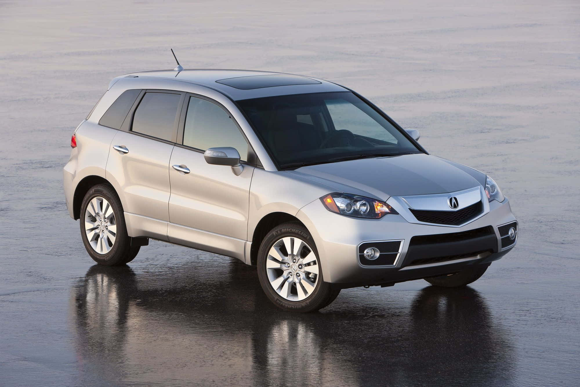 Acura Rdx 桌布 壁紙 — 一輛時尚的銀色Acura SUV在柔和日光下映照在潮濕的瀝青路面上。