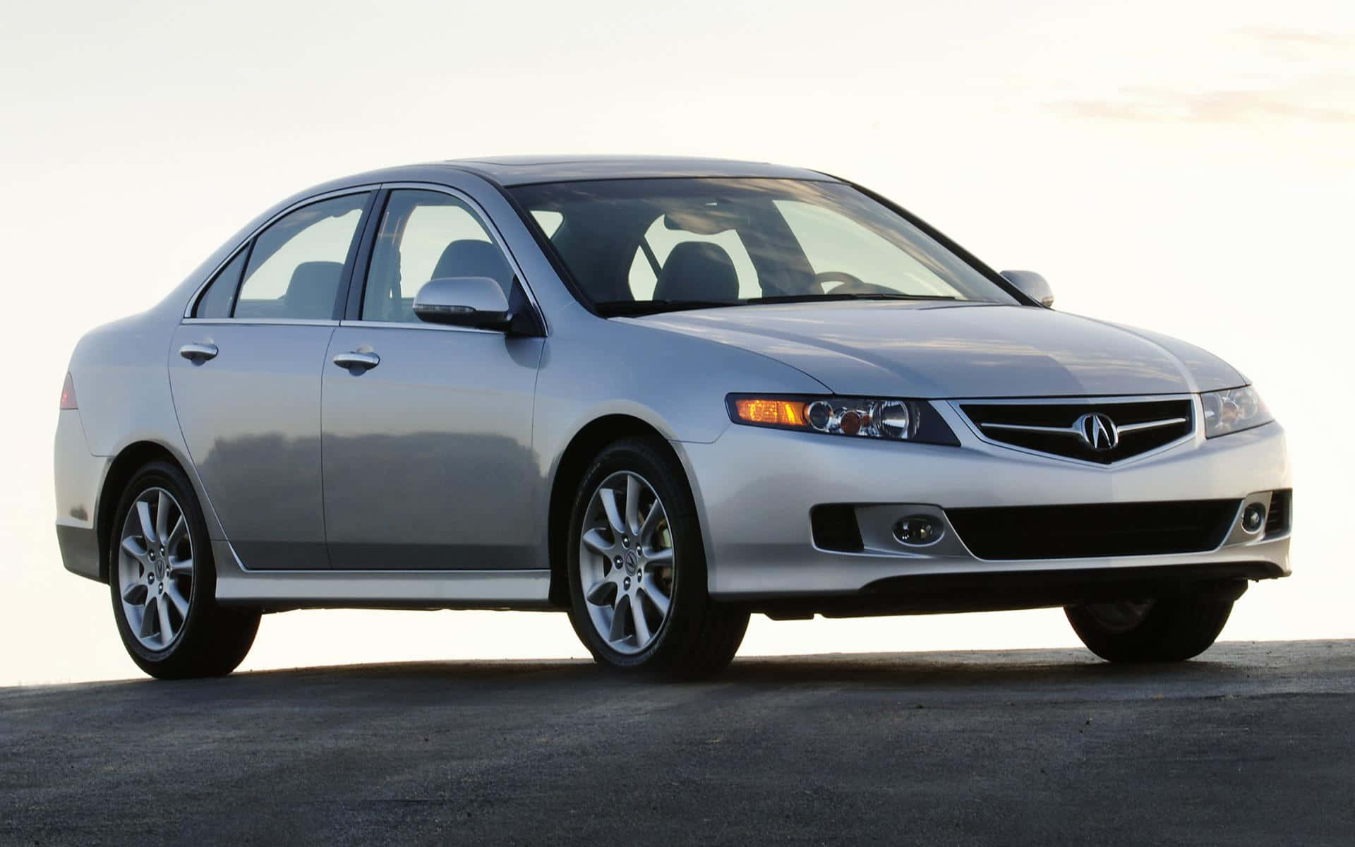 Acura Tsx 桌布 壁紙 — 一輛時尚的銀色Acura轎車停在瀝青路上，低垂的太陽散發柔和金色光芒，投下輕柔的陰影。