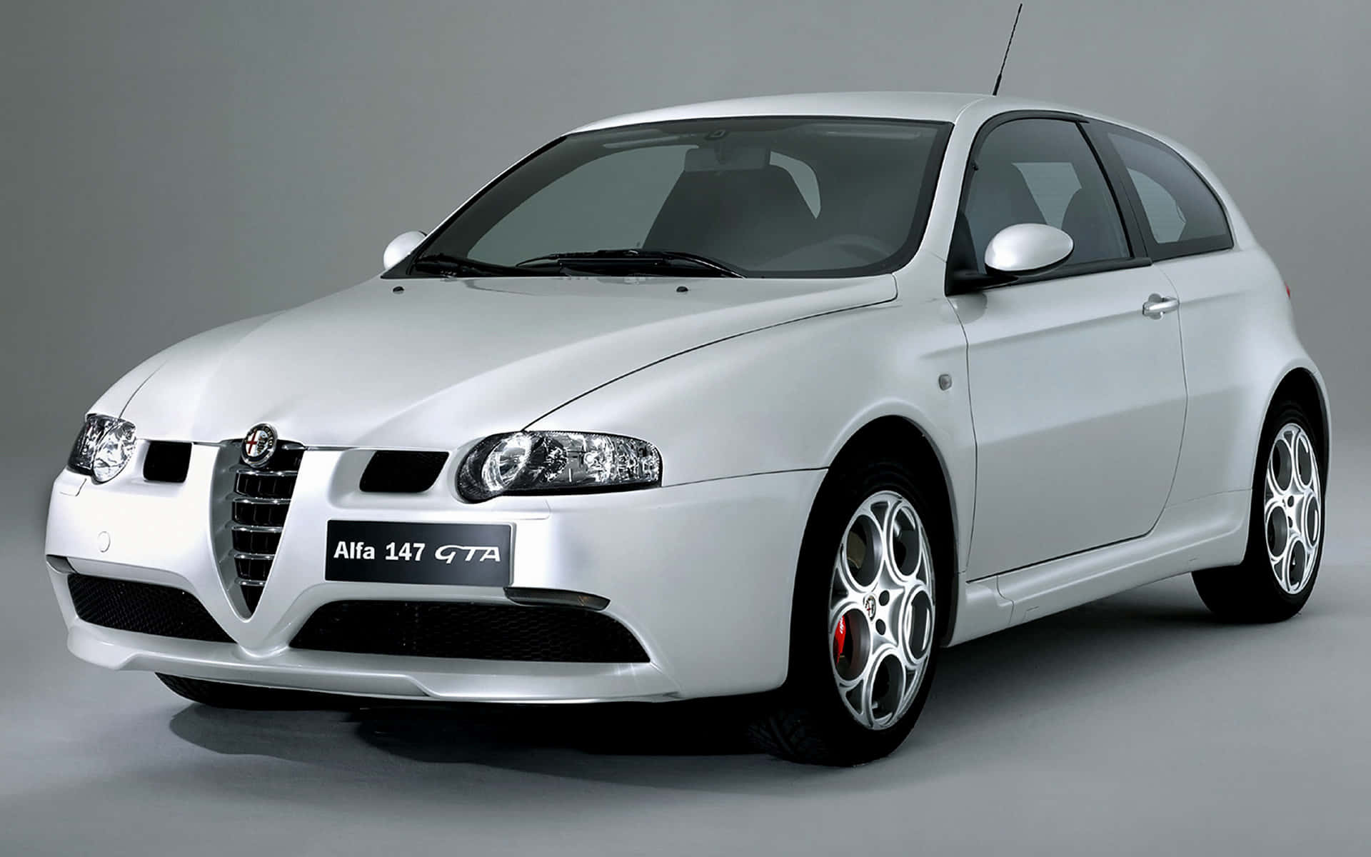 Alfa Romeo 147 桌布 壁紙 — 一輛時尚的銀色Alfa 147 GTA跑車，配備紅色制動卡鉗和合金輪圈，在灰色中性工作室背景前展示。
