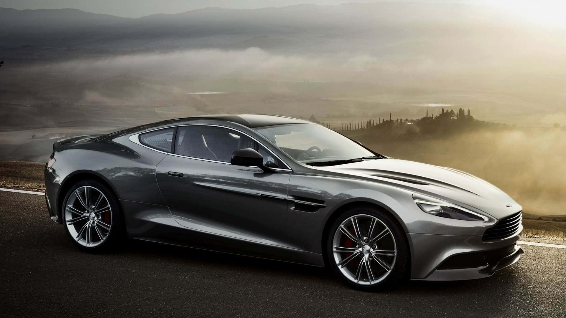 Aston Martin Rapide S 桌布 壁紙 — 一輛時尚的銀色Aston Martin跑車在黃金時段沿著蜿蜒的道路穿過霧氣瀰漫的山谷。
