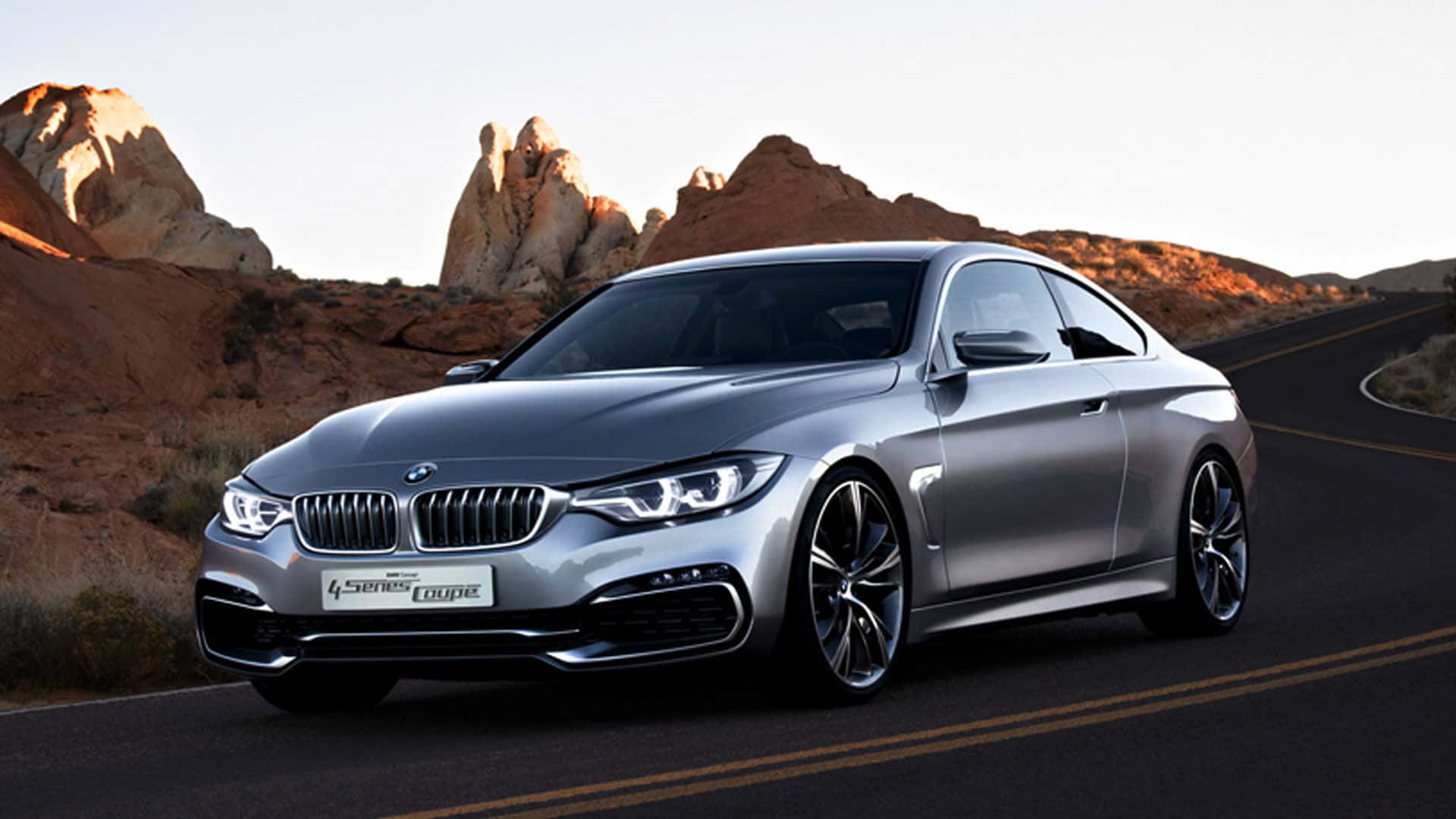 Bmw 4 Series 桌布 壁紙 — 一輛時尚的銀色BMW 4 Series Coupe在晴朗天空下，沿著沙漠道路行駛，兩旁是紅色岩層。
