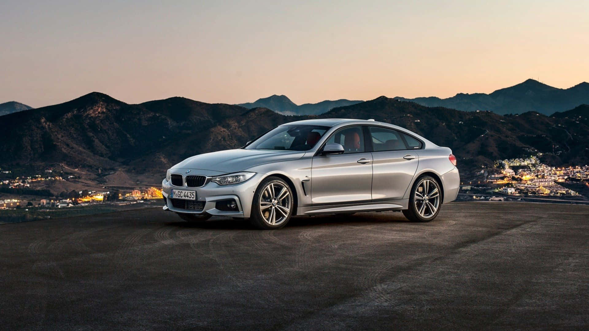 Bmw 4 Series 桌布 壁紙 — 一輛時尚的銀色BMW 4系轎跑車在黃昏時停在山頂上，下方是山脈和燈火通明的城鎮。