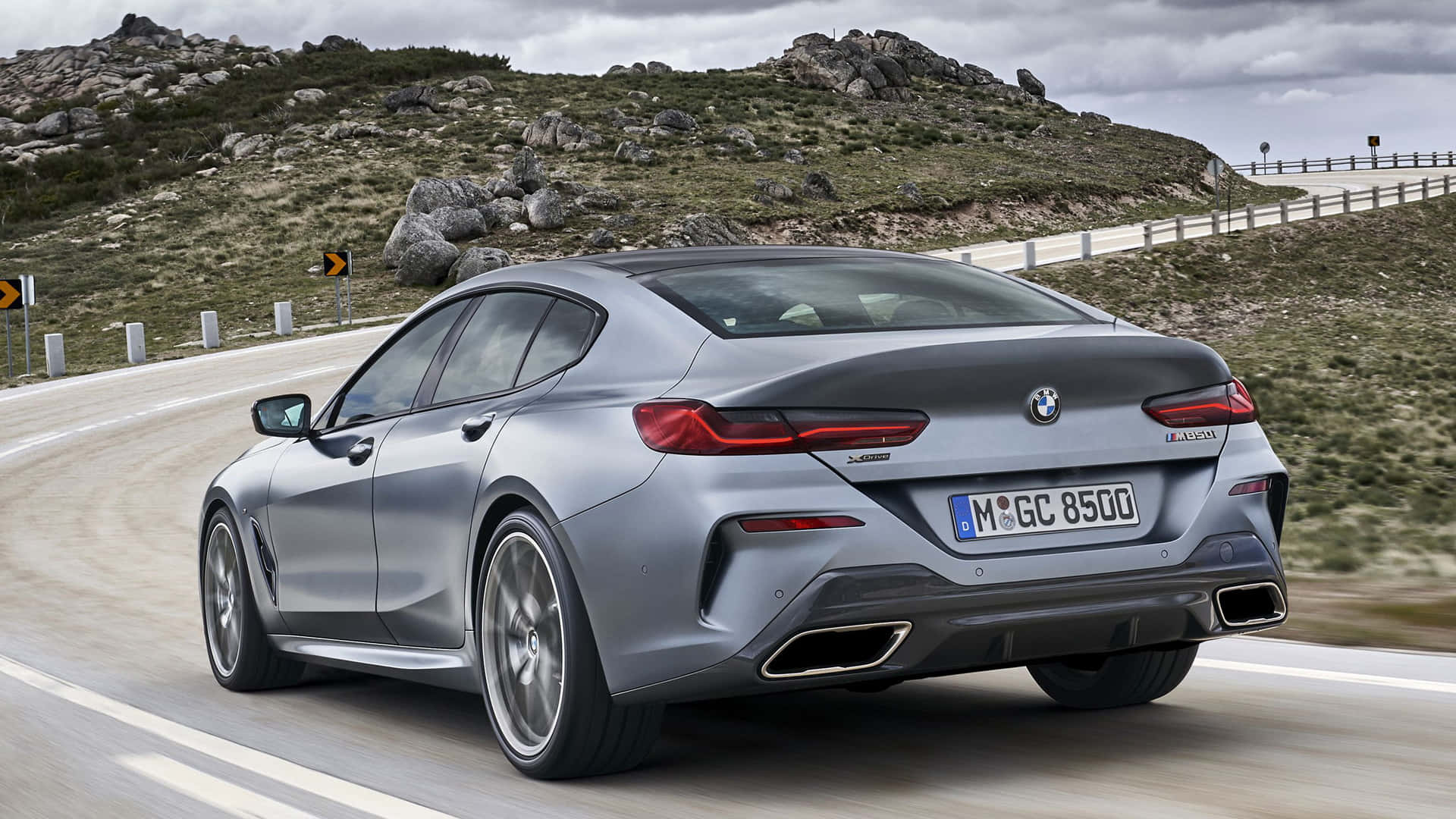 Bmw 8 Series 桌布 壁紙 — 一輛時尚的銀色BMW 8系Gran Coupe沿著蜿蜒的山路行駛，地形崎嶇，天空多雲。
