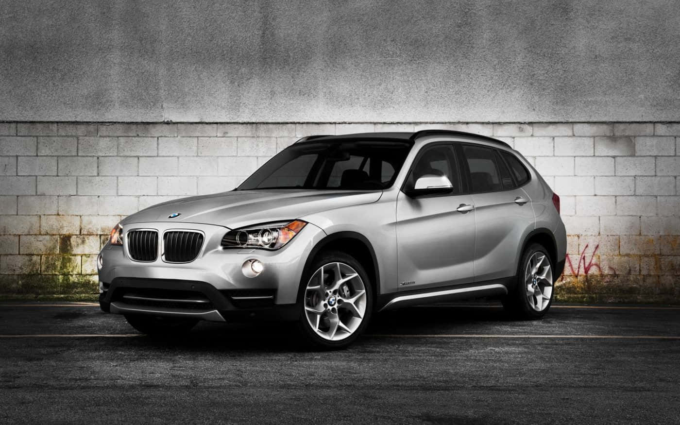 Bmw X1 桌布 壁紙 — 一輛時尚的銀色BMW X1 SUV停泊在經風化的混凝土牆旁，牆上有塗鴉。