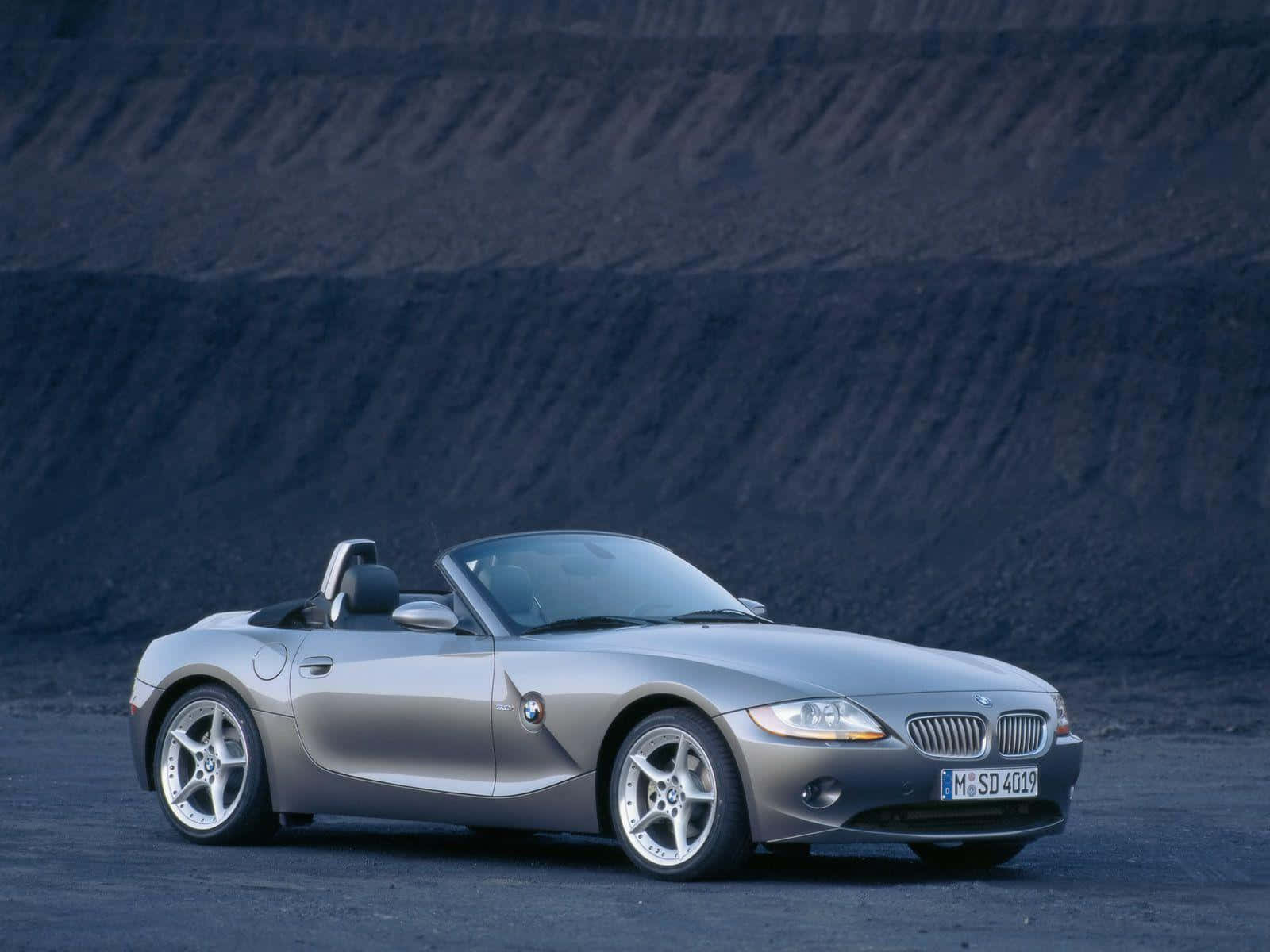 Bmw Z4 桌布 壁紙 — 一輛時尚的銀色BMW Z4敞篷跑車停在深色碎石上，前方是高聳的木炭色採石場牆壁。