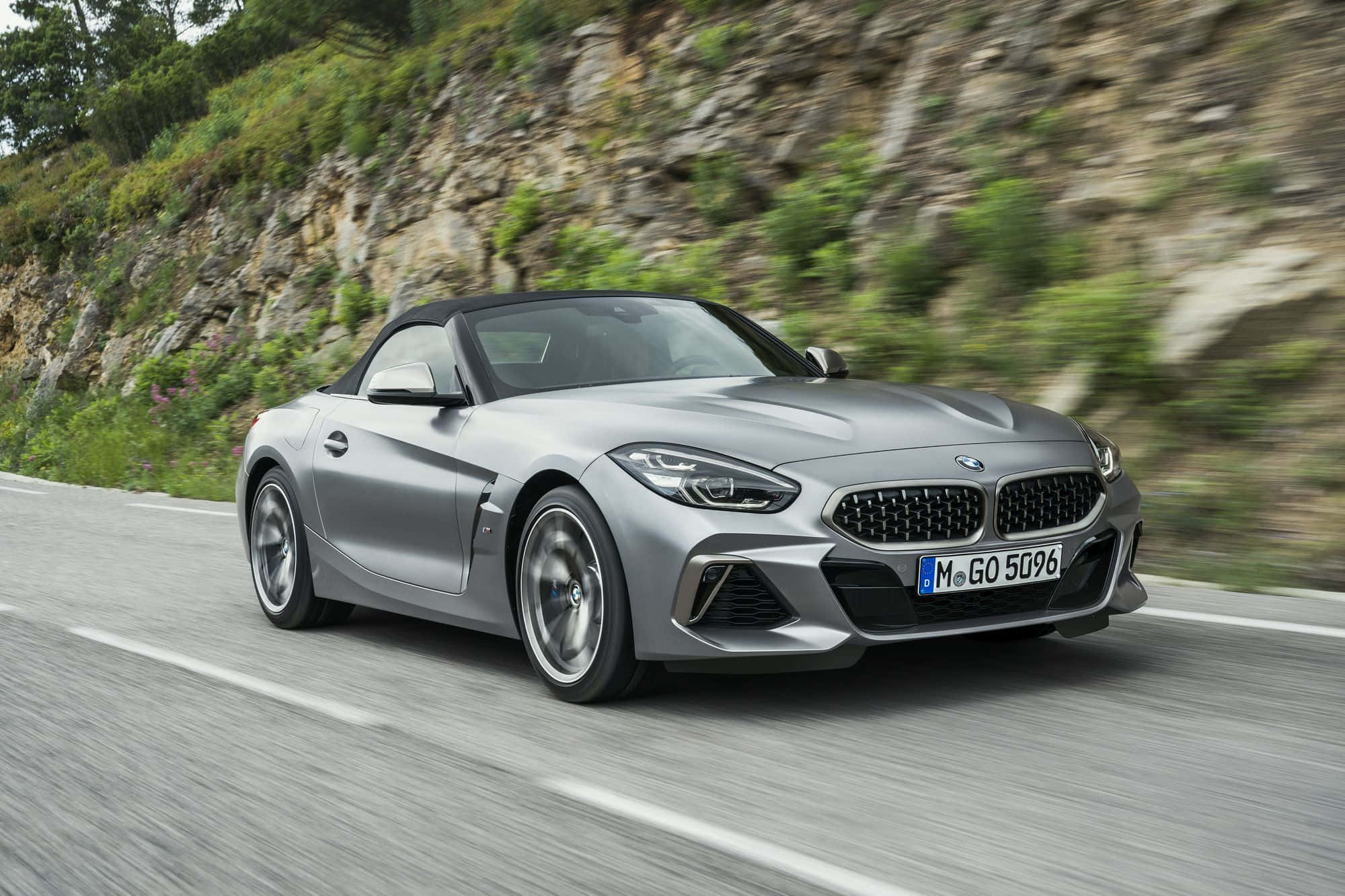Bmw Z4 桌布 壁紙 — 一輛時尚的銀色BMW Z4開篷跑車在蜿蜒的山路上飛馳，背景是模糊的綠植和岩石峭壁。