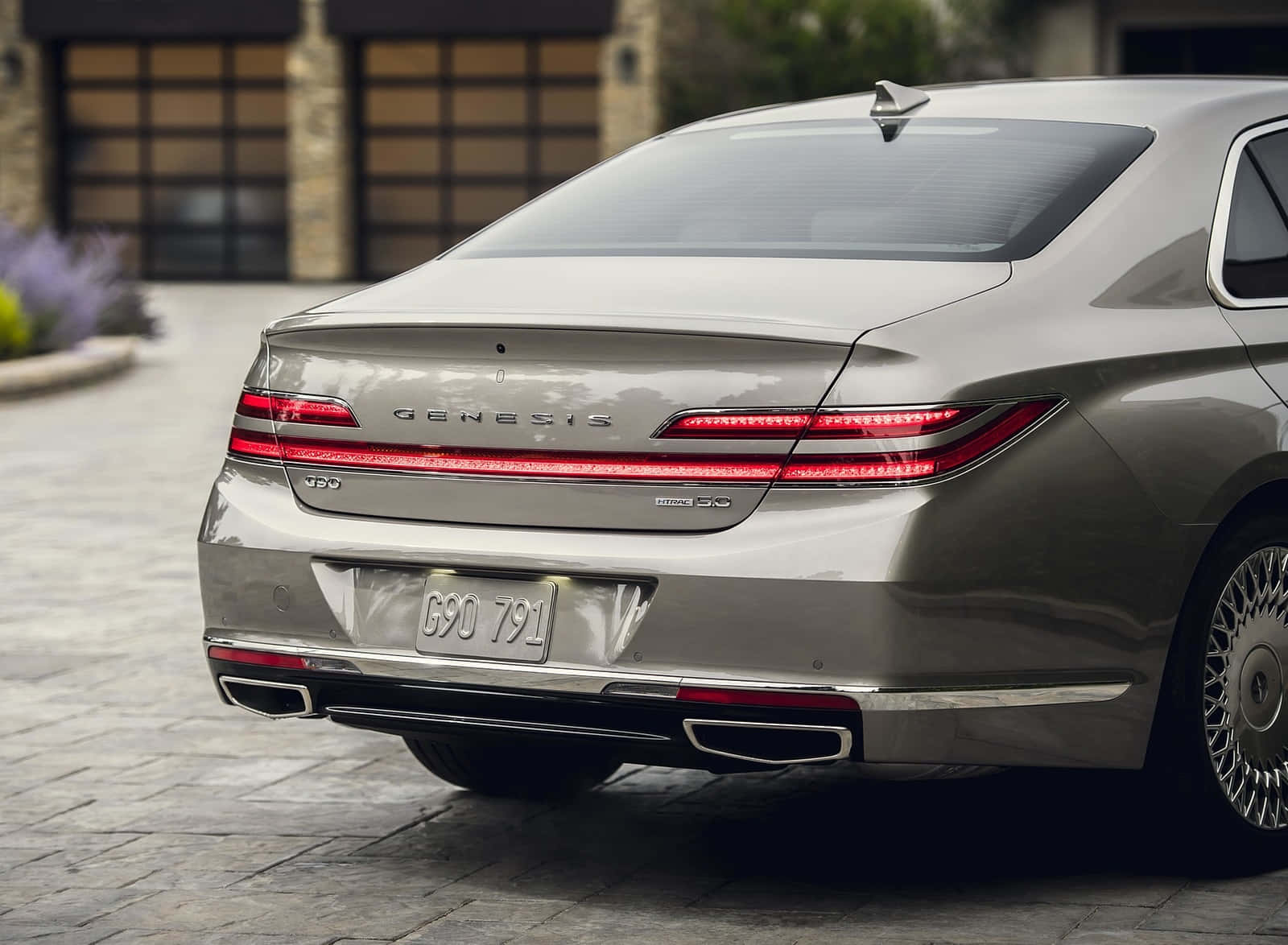 Genesis G90 桌布 壁紙 — 一輛時尚的銀色Genesis G90轎車，帶有發光的紅色尾燈，停在現代房屋附近的石頭車道上。