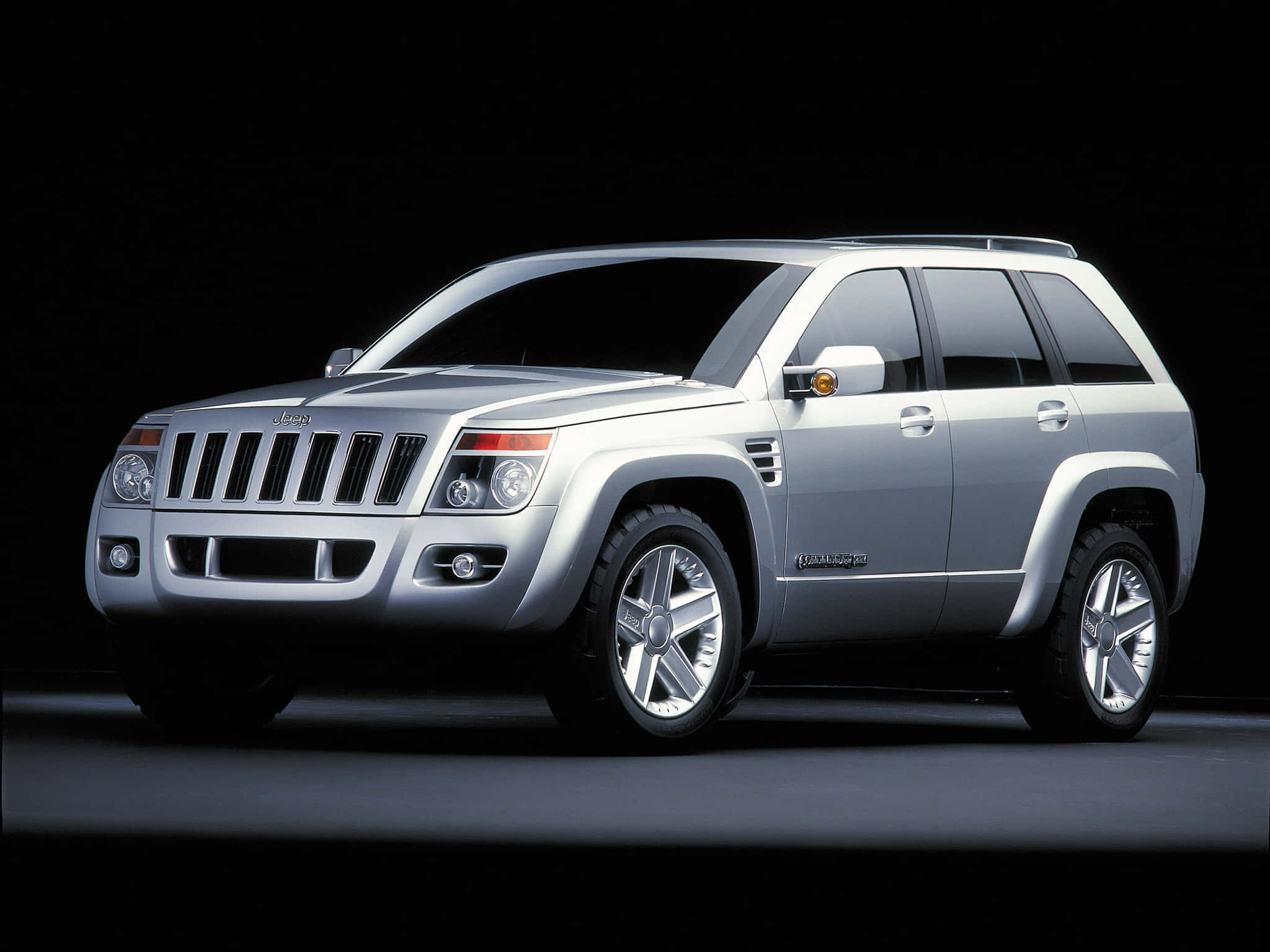 Jeep Commander 桌布 壁紙 — 一輛時尚的銀色Jeep Grand Cherokee概念SUV在黑色背景下的戲劇性工作室聚光燈中展示。