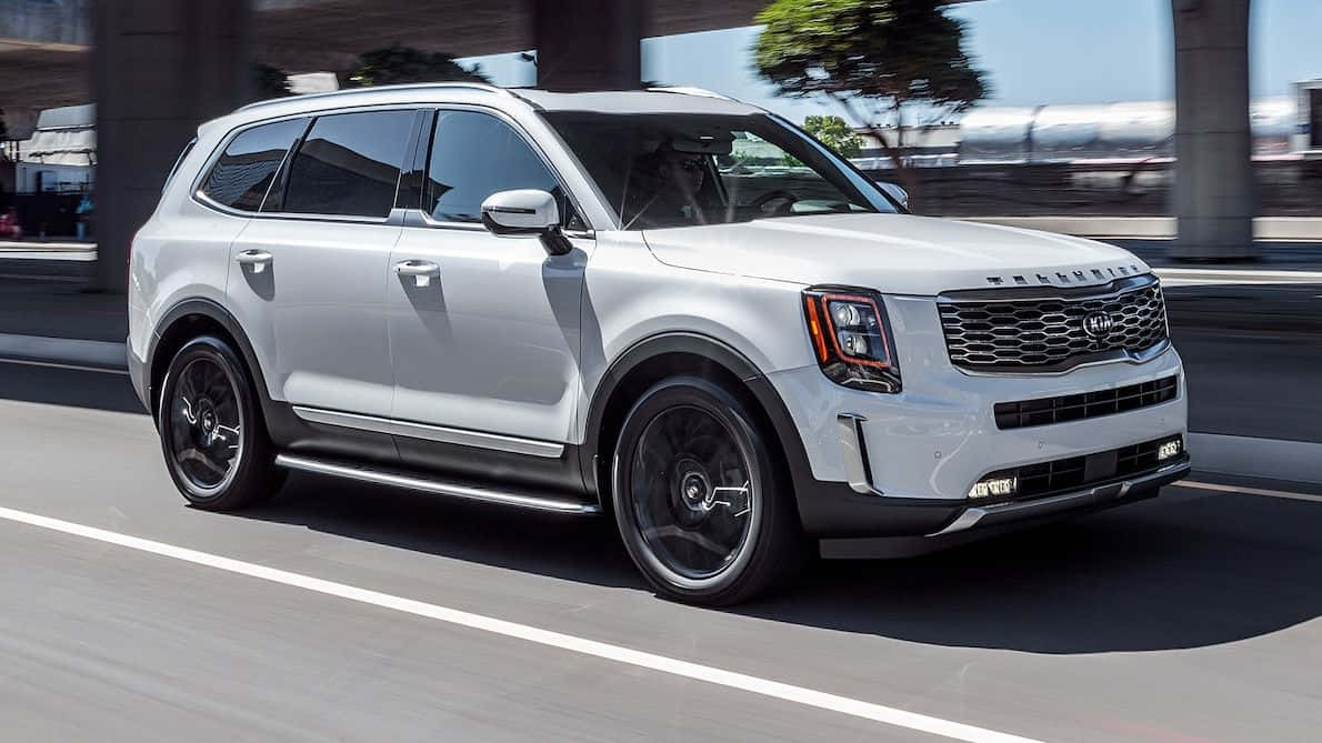 Family Car 桌布 壁紙 — 一輛時尚的銀色Kia Telluride SUV在陽光明媚的城市高速公路上巡航，車輪和背景帶有動態模糊效果。