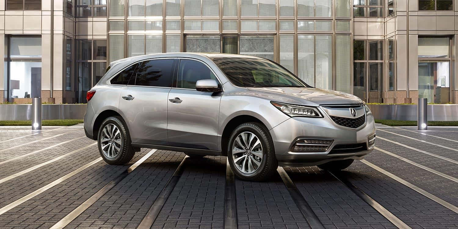 Acura Mdx 桌布 壁紙 — 一輛時尚的銀色SUV停泊在現代磚砌廣場上，前方是玻璃幕牆的都市建築。