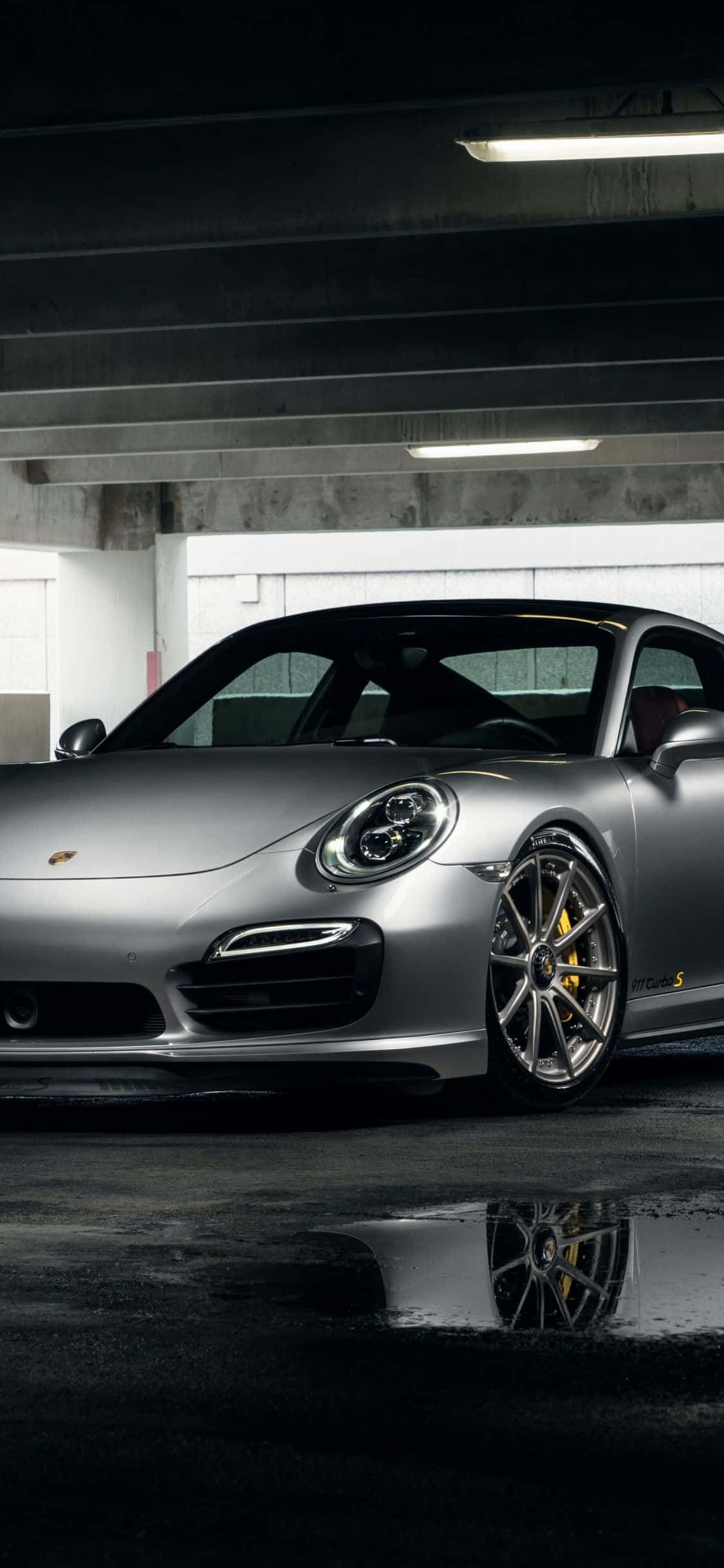 Porsche iPhone 桌布 壁紙 — 一輛時尚的銀色保時捷911 GT3 S停泊在光線昏暗的地下停車場，濕漉漉的混凝土反射著車輪。
