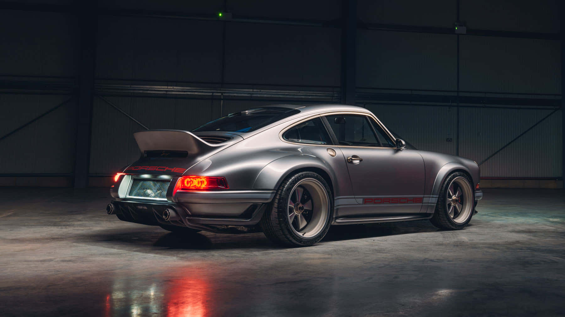 Back 桌布 壁紙 — 一輛時尚的銀色保時捷911 Turbo，紅色尾燈閃爍，停在昏暗的工業車庫中。