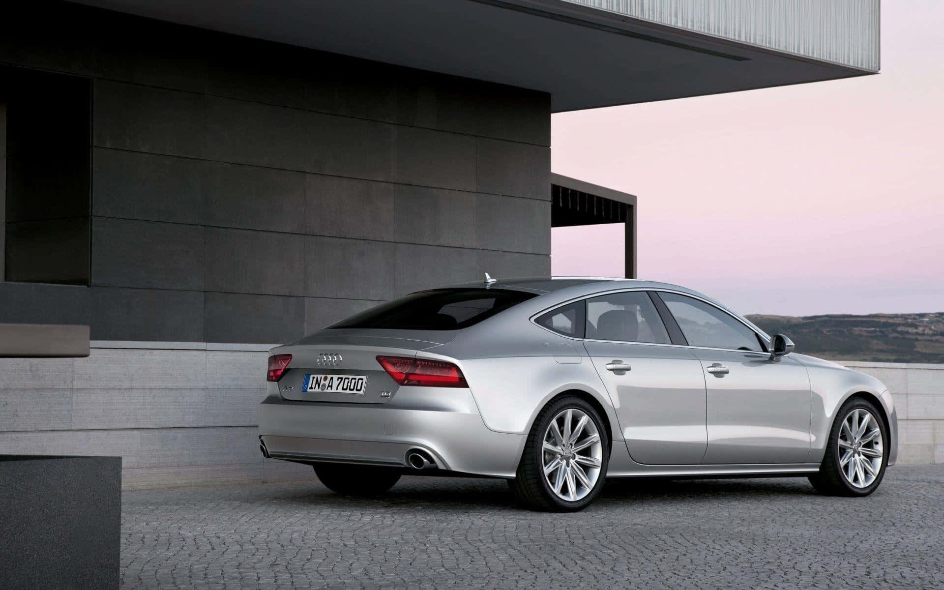 Audi S7 桌布 壁紙 — 一輛時尚的銀色奧迪A7 Sportback在黃昏時停泊在現代混凝土建築旁邊的鵝卵石車道上。