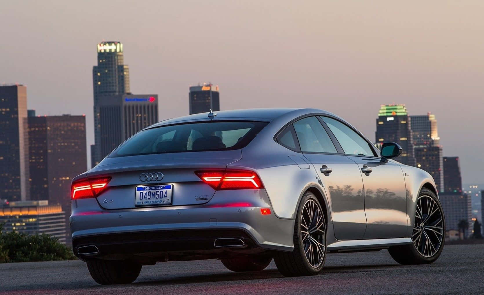 Audi S7 桌布 壁紙 — 一輛時尚的銀色奧迪A7轎車停在城市觀景點，尾燈發光，映襯著暮色中燈火通明的摩天大樓天際線。