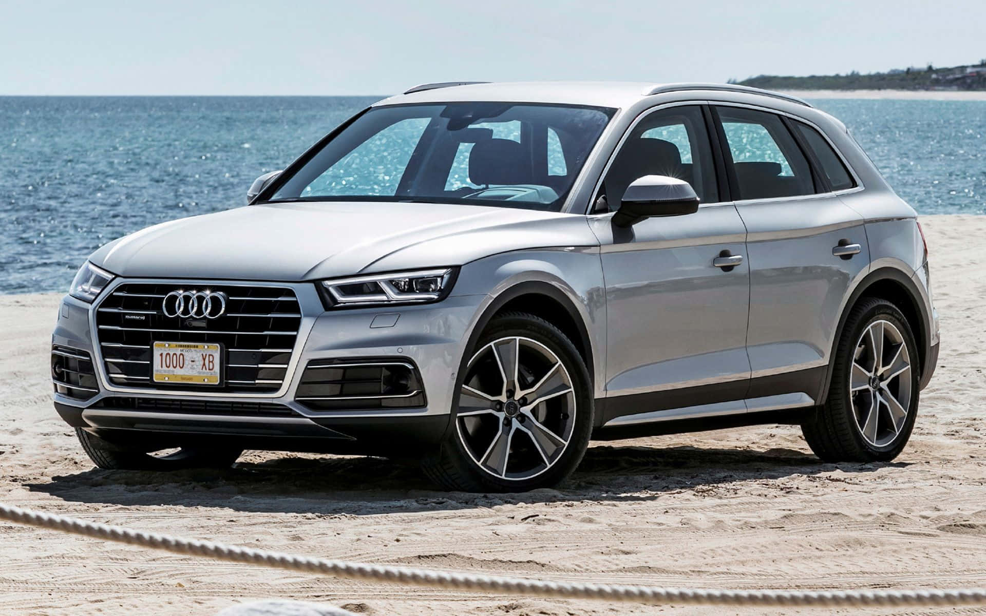 Audi Sq5 桌布 壁紙 — 一輛時尚的銀色奧迪Q5 SUV停在陽光明媚的沙灘上，背景是海浪。