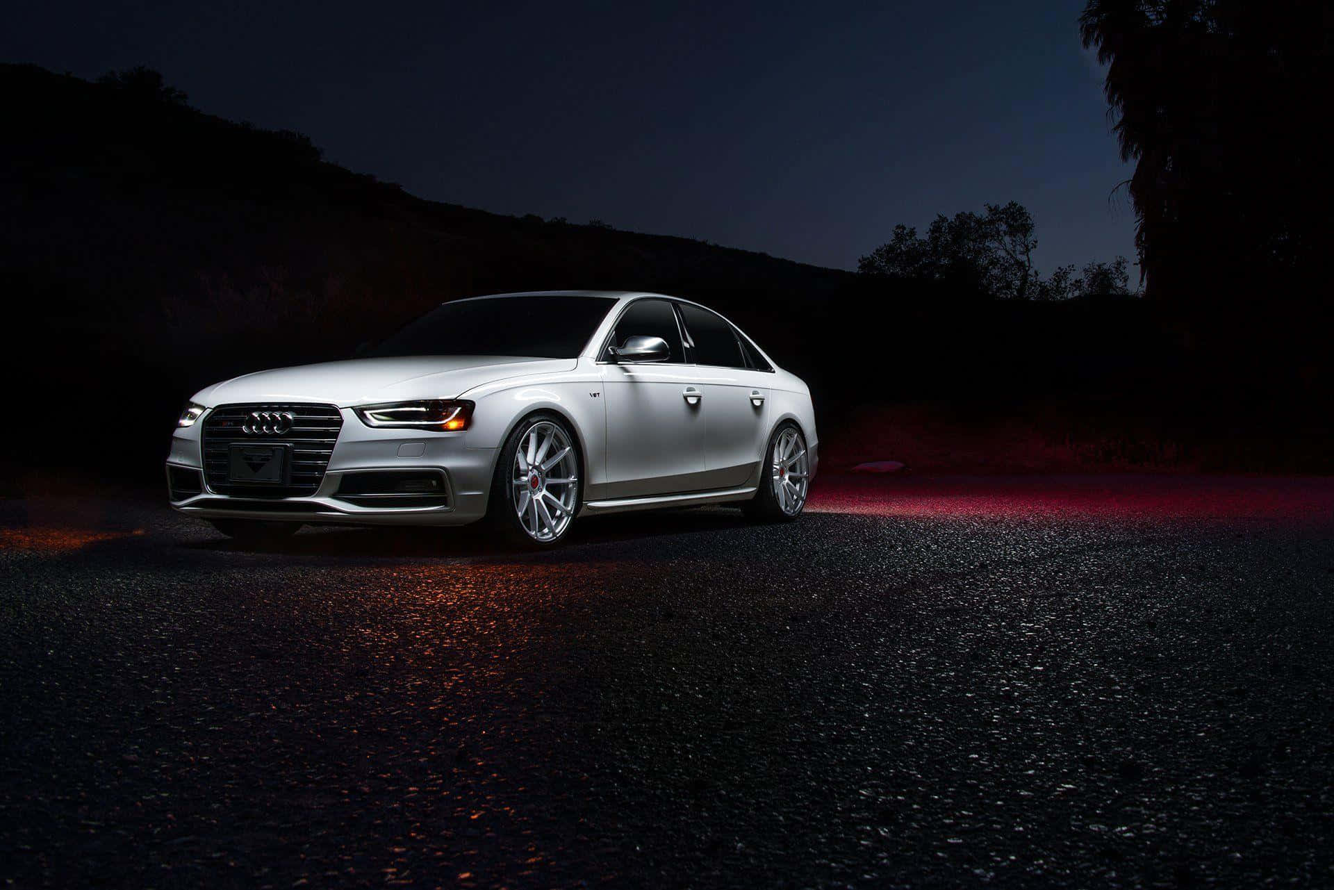 Audi S4 桌布 壁紙 — 一輛時尚的銀色奧迪轎車在戲劇性的夜間燈光下，在黑暗的道路上閃耀著紅色光芒的倒影。