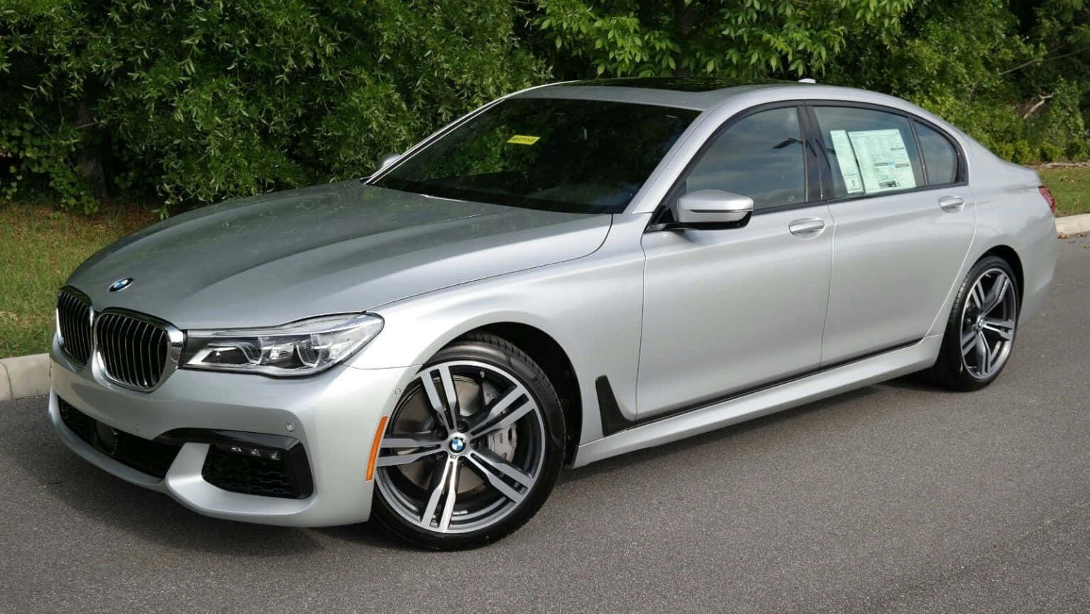 Bmw 7 Series 桌布 壁紙 — 一輛時尚的銀色寶馬7系轎車停在瀝青路面上，背景是茂密的綠色灌木叢。