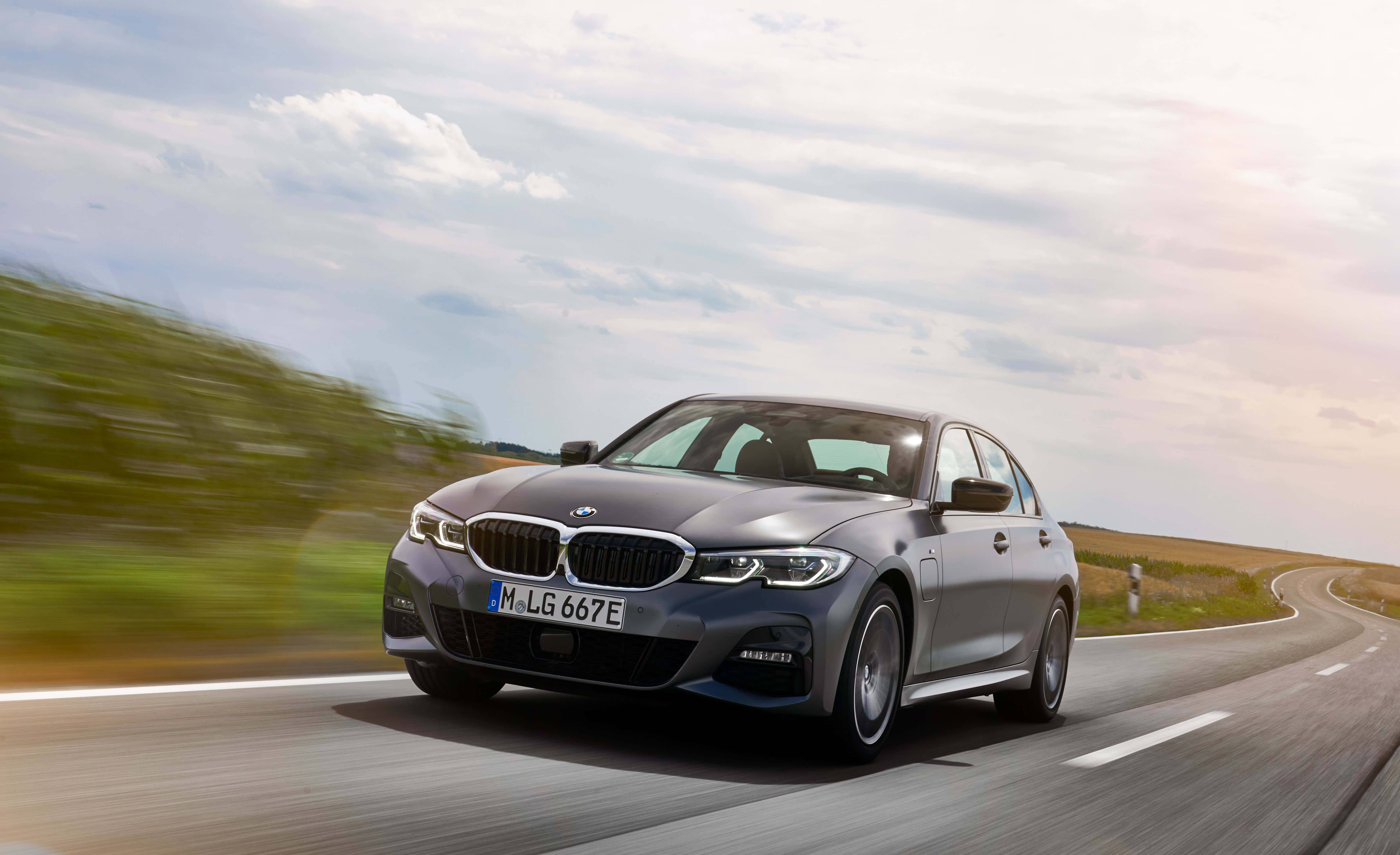 Bmw 3 Series 桌布 壁紙 — 一輛時尚的銀色寶馬房車在部分多雲的天空下，沿著蜿蜒的鄉村道路疾馳，周圍環境帶有動態模糊效果。