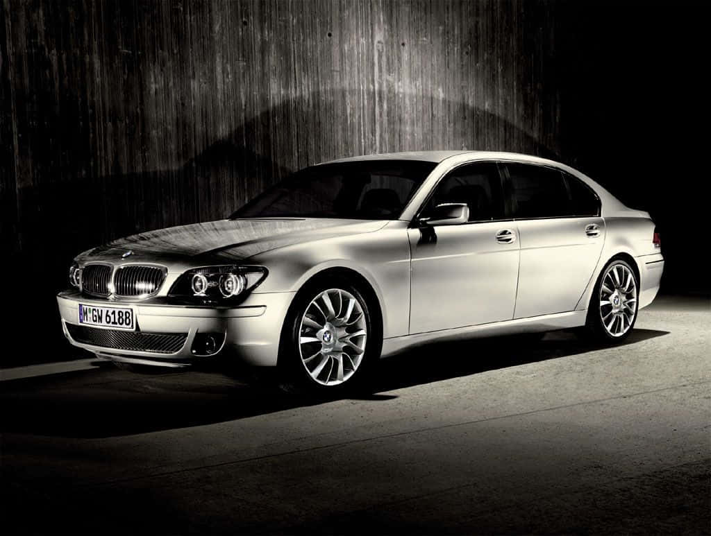 Bmw 7 Series 桌布 壁紙 — 一輛時尚的銀色寶馬轎車在戲劇性的聚光燈下，在黑暗紋理牆壁前閃閃發光，營造出陰鬱的攝影棚氛圍。