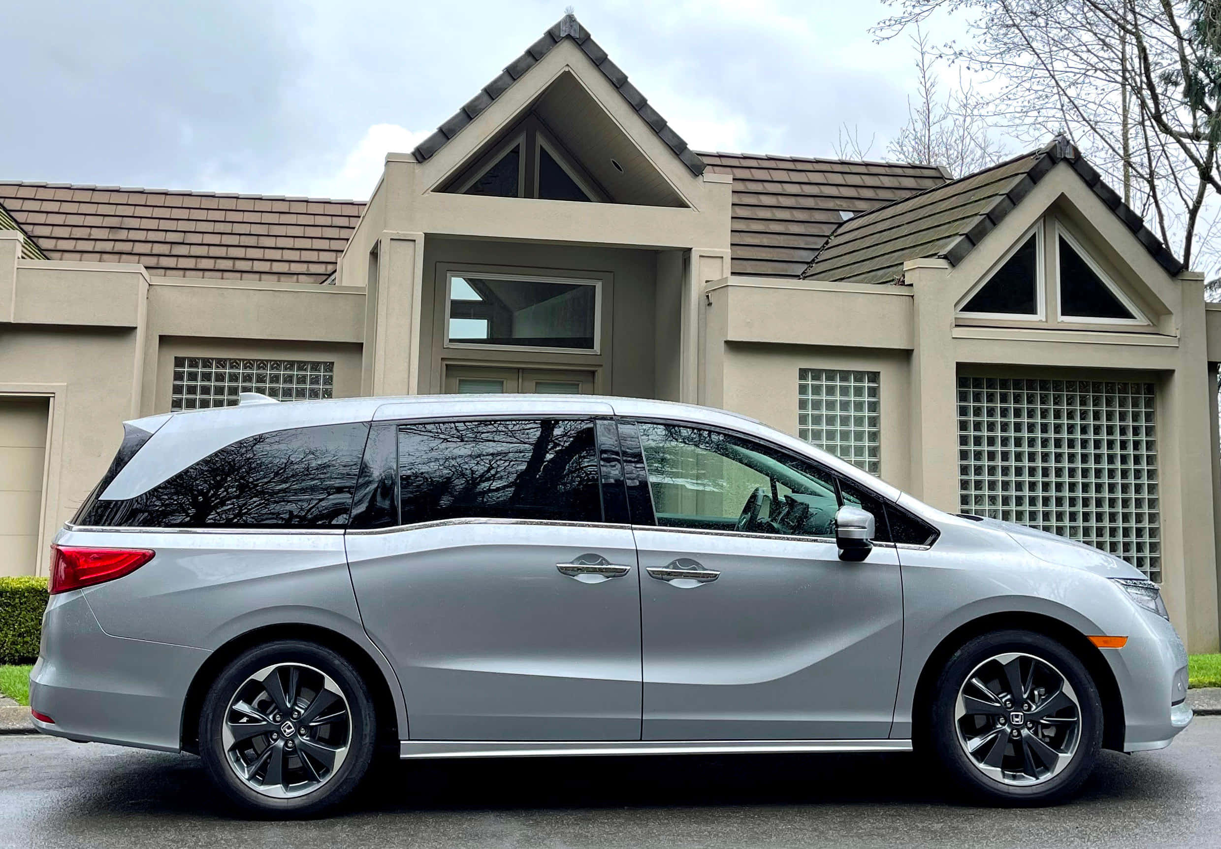 Honda Odyssey 桌布 壁紙 — 一輛時尚的銀色小型貨車停在一棟米色房屋前，房屋有玻璃磚窗，天空多雲。
