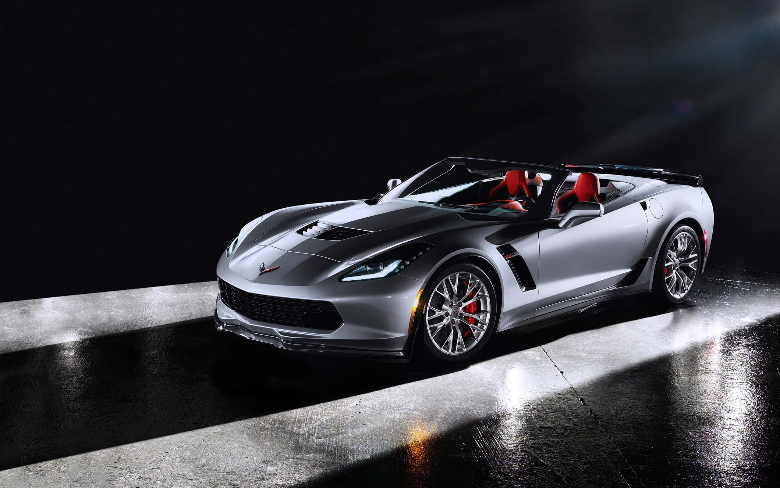 Chevrolet Corvette Z06 桌布 壁紙 — 一輛時尚的銀色敞篷跑車，紅色內飾，在潮濕的混凝土地板上，在戲劇性的聚光燈下閃閃發光。