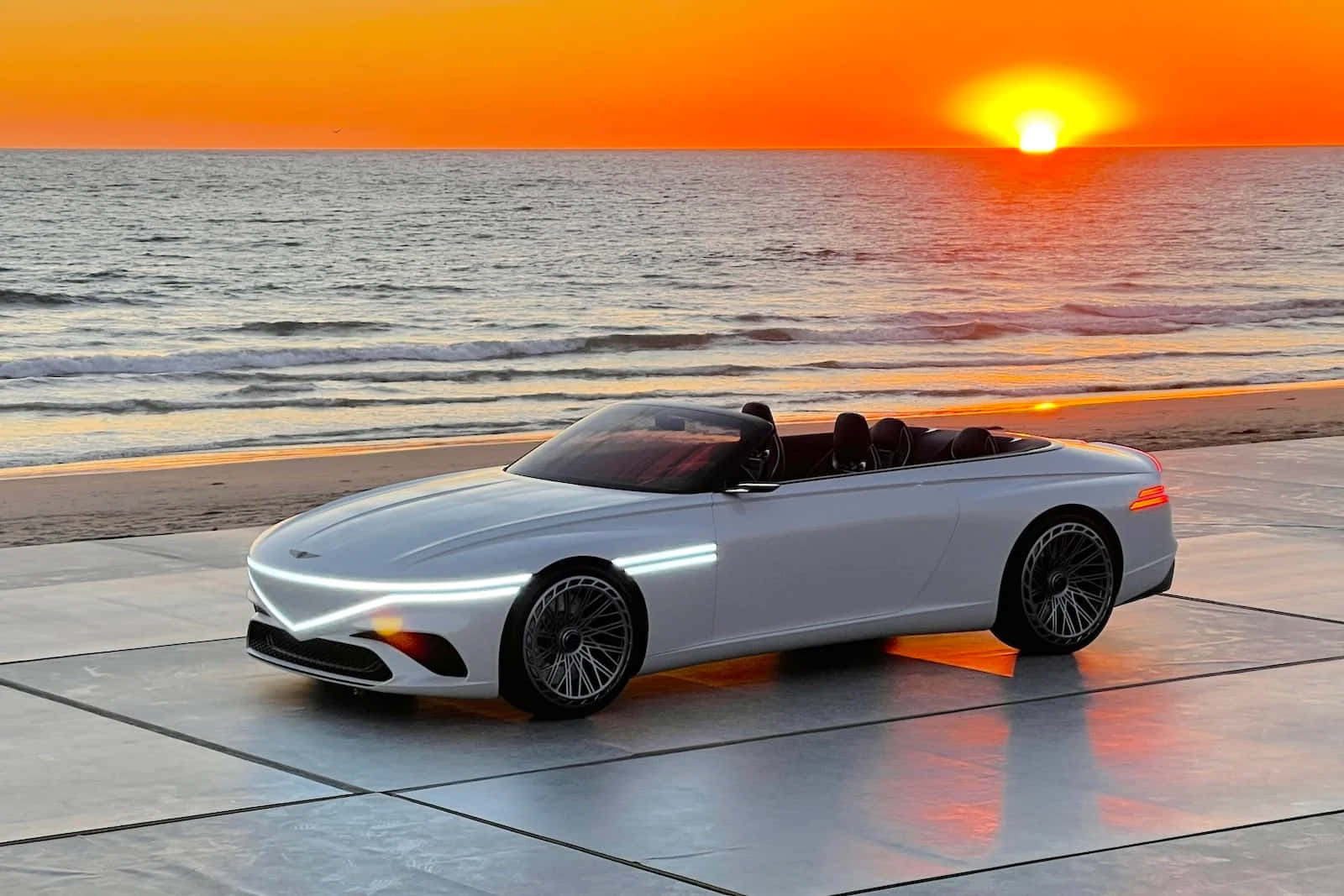 Genesis X Concept 桌布 壁紙 — 一輛時尚的銀色敞篷跑車在夕陽下的瓷磚海灘上閃閃發光，天空呈現橙色，海浪拍打。
