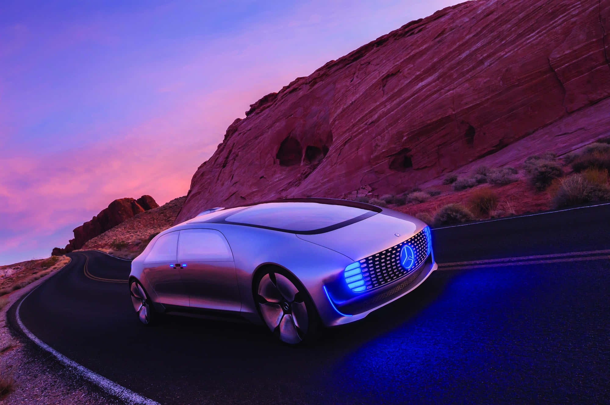 Car Technology 桌布 壁紙 — 一輛時尚的銀色未來感汽車，帶有發光的藍色車頭燈，在充滿活力的紫色和粉紅色日落天空下沿著沙漠道路蜿蜒行駛。