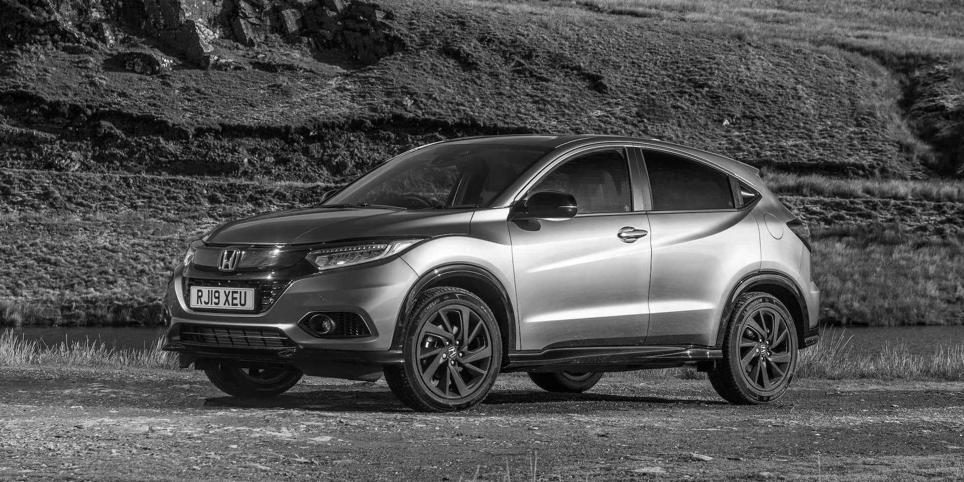 Honda Hr-v 桌布 壁紙 — 一輛時尚的銀色本田HR-V SUV停泊在碎石路上，旁邊是單色調的草地山坡。