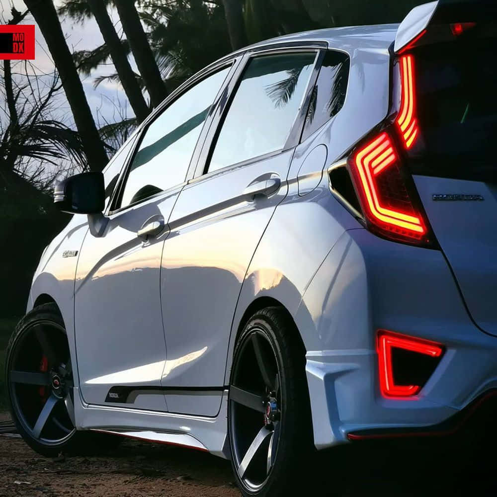 Honda Fit 桌布 壁紙 — 一輛時尚的銀色本田Jazz，在黃昏時分停在棕櫚樹下，紅色尾燈閃閃發光。