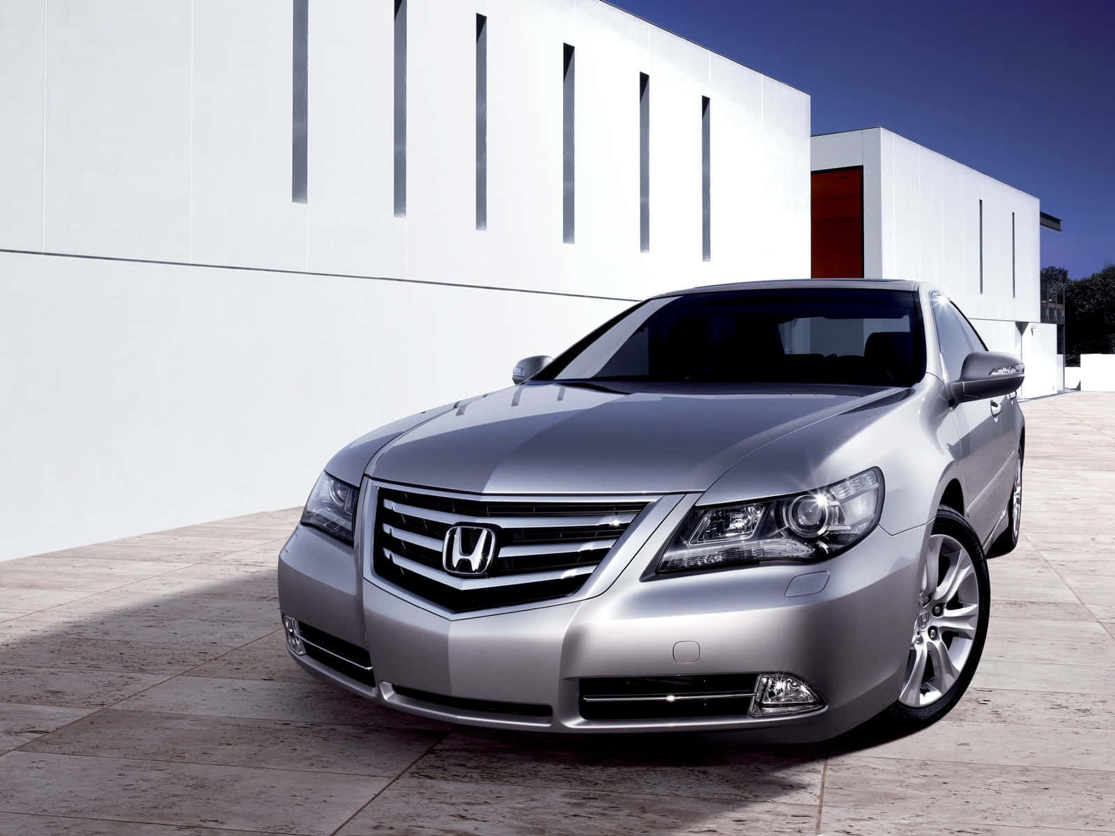 Honda Legend 桌布 壁紙 — 一輛時尚的銀色本田豪華轎車停放在瓷磚庭院上，旁邊是一座現代白色建築，在清澈的藍天下。
